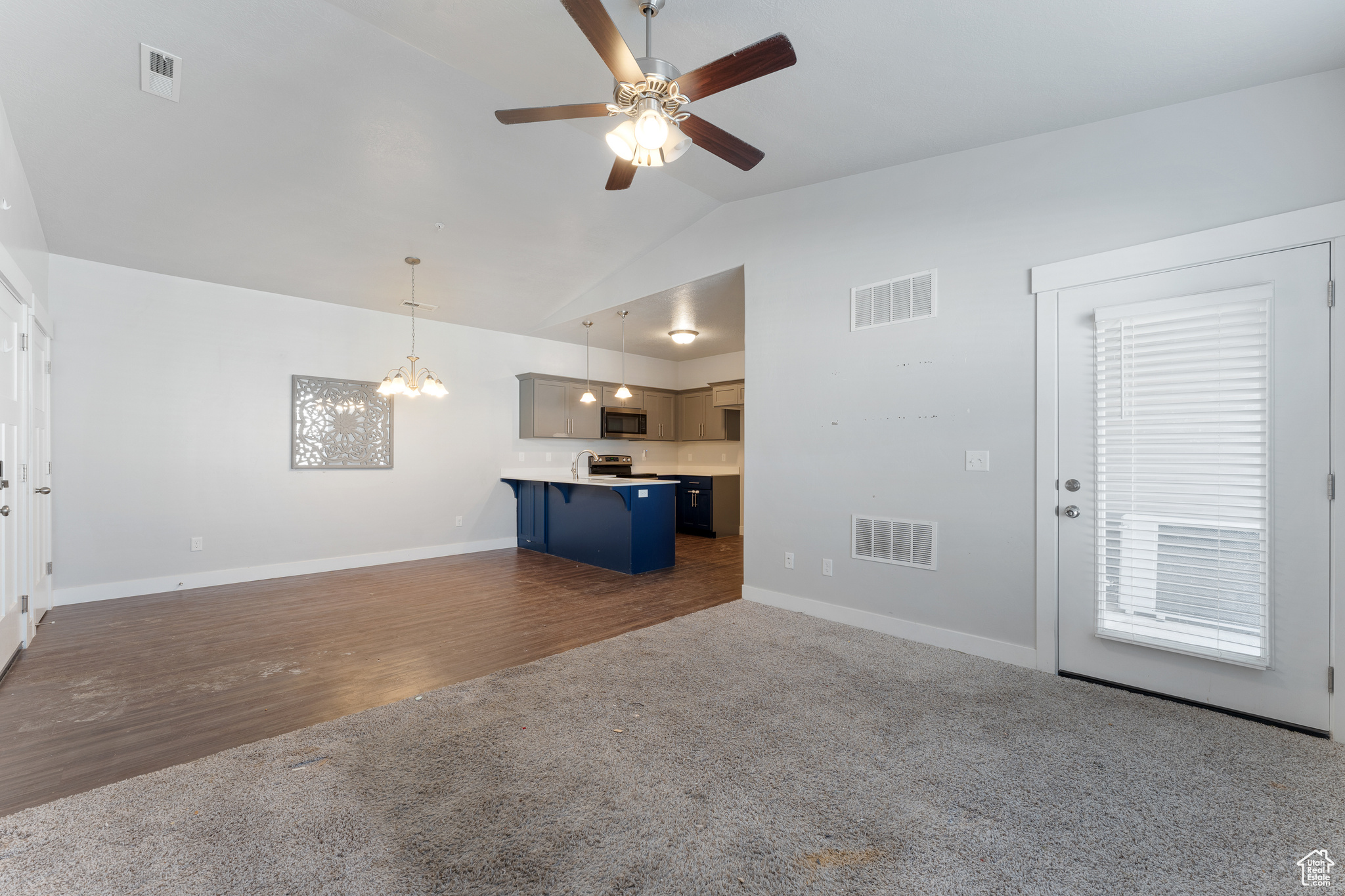Unfurnished living room featuring lofted ceiling, ceiling fan with notable chandelier, and dark carpet