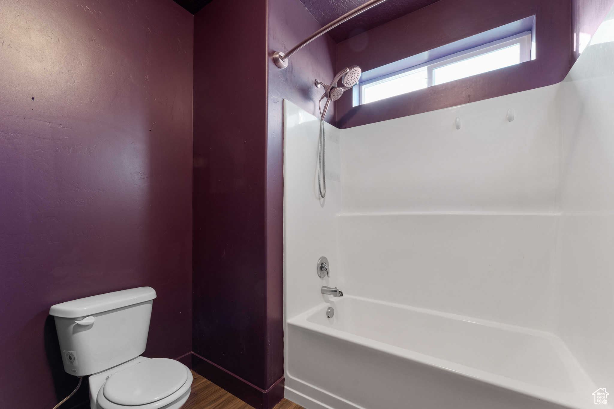 Bathroom with hardwood / wood-style flooring, washtub / shower combination, and toilet