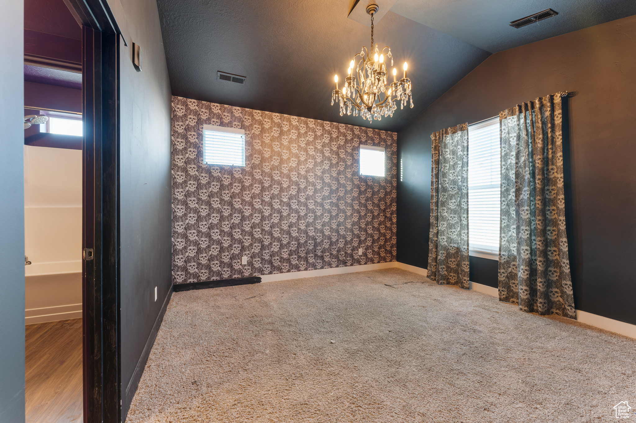 Empty room with lofted ceiling, a notable chandelier, and carpet floors