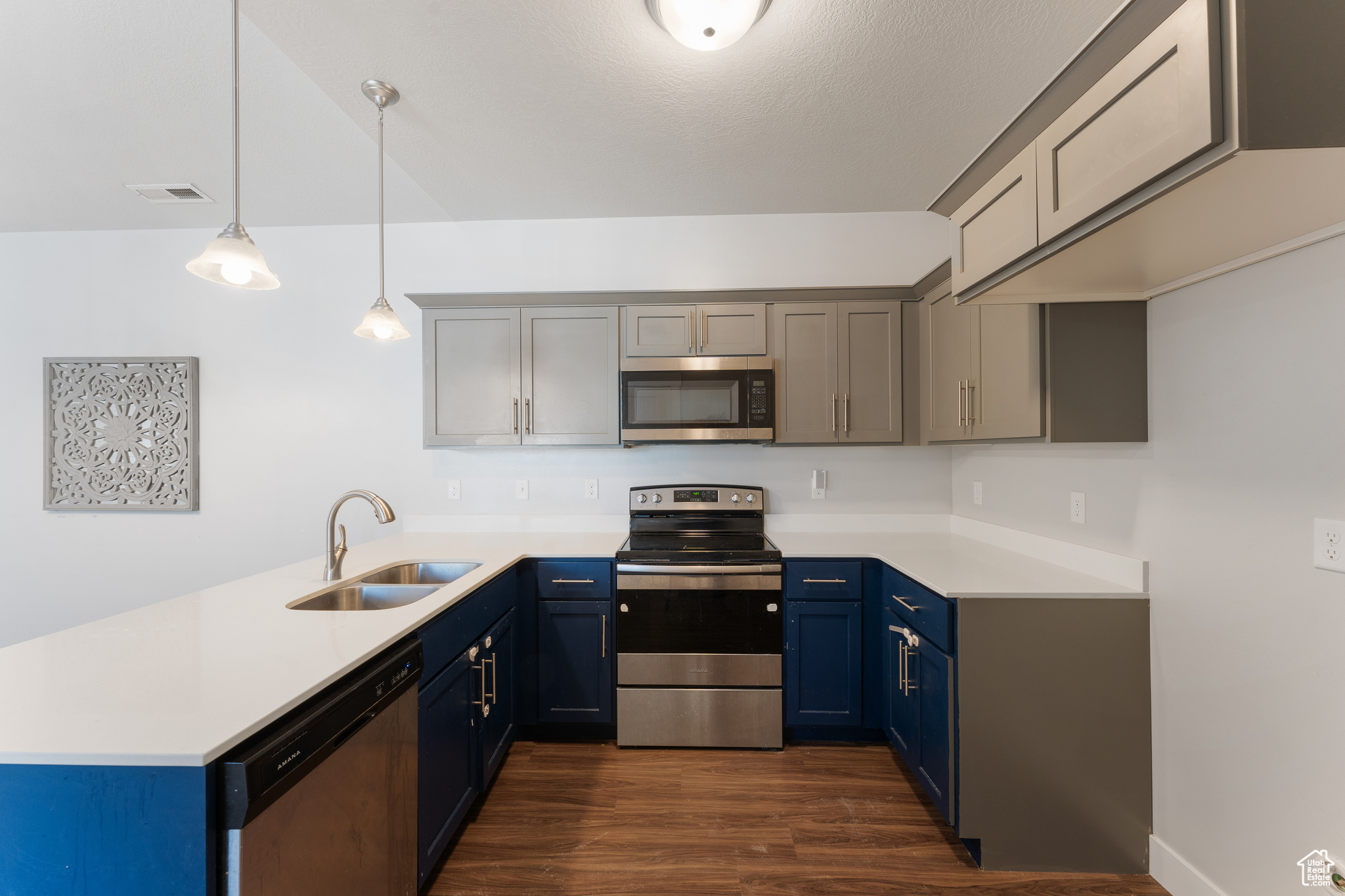 Kitchen featuring appliances with stainless steel finishes, decorative light fixtures, blue cabinets, sink, and dark wood-type flooring