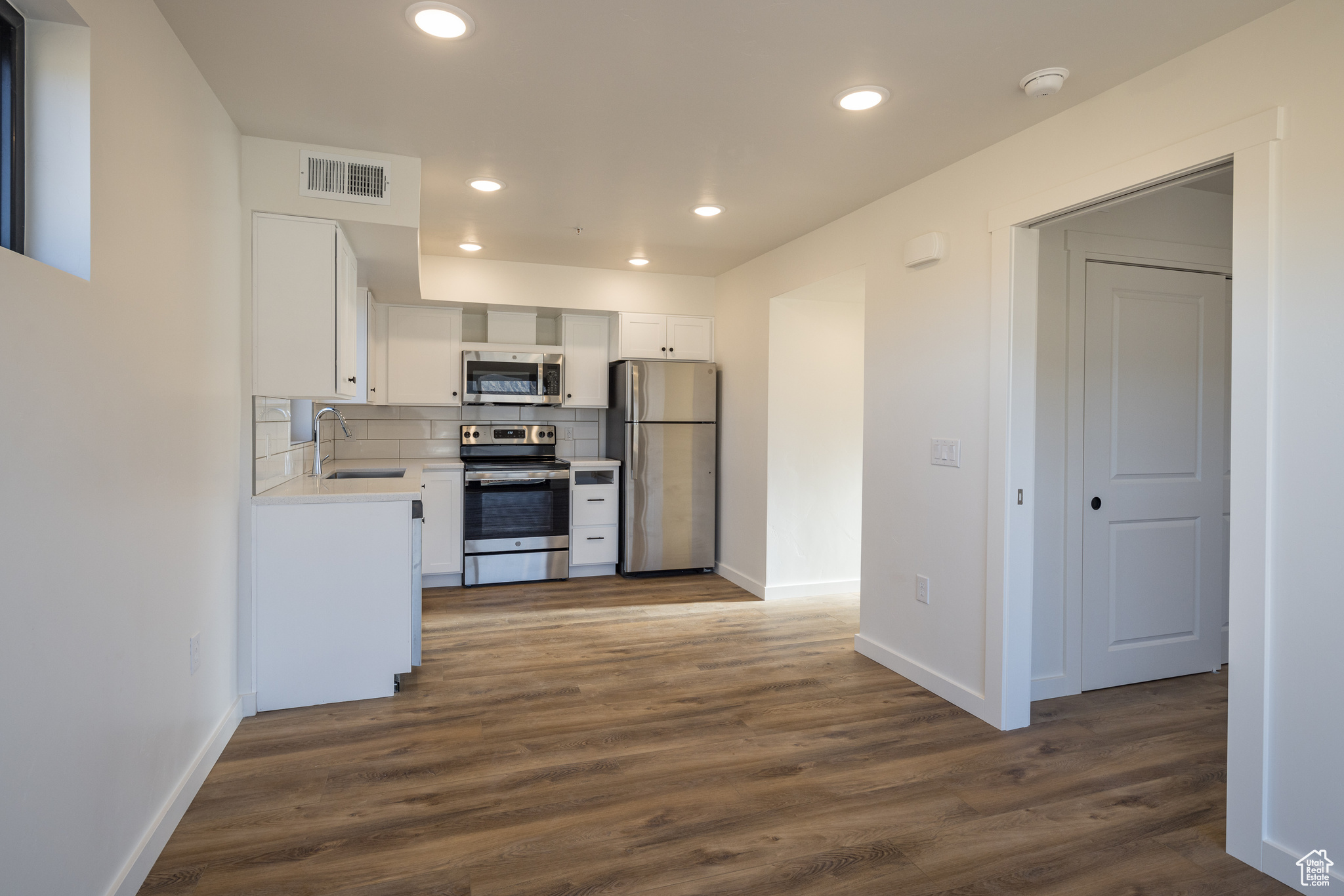 Kitchen with sink, appliances with stainless steel finishes, white cabinetry, dark hardwood / wood-style floors, and decorative backsplash