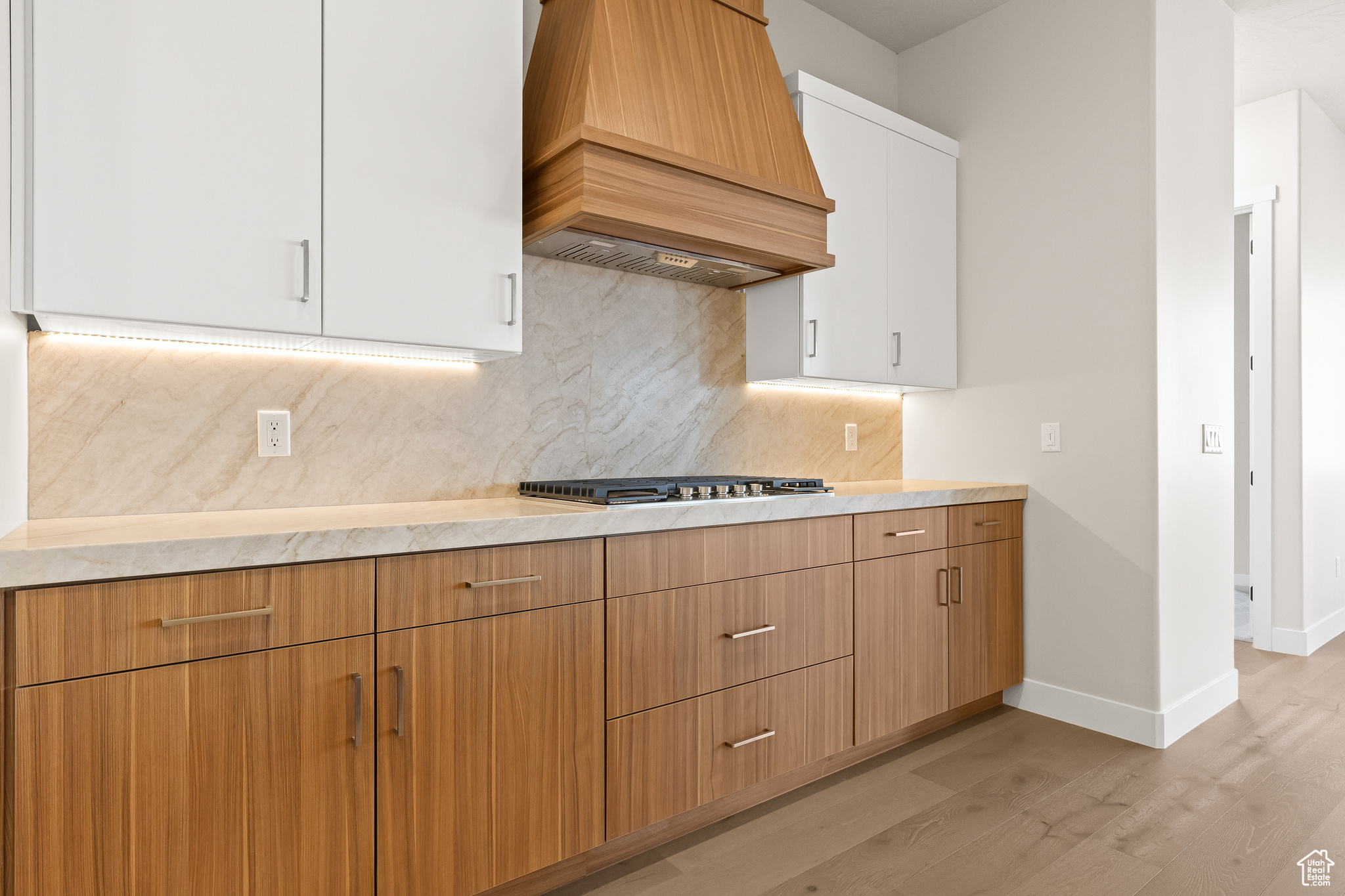 Kitchen featuring premium range hood, decorative backsplash, stainless steel gas stovetop, and light countertops