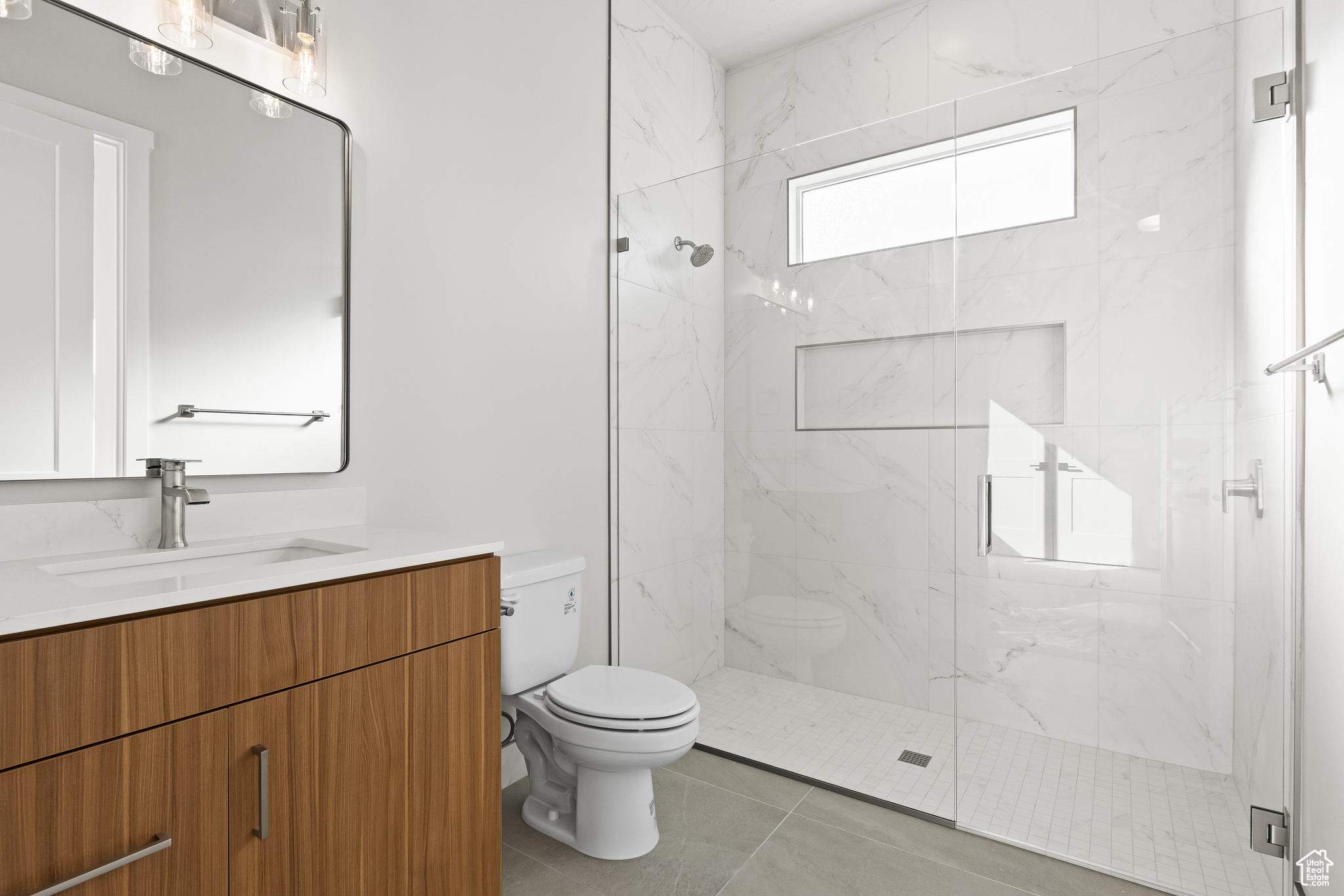 Full bath featuring a marble finish shower, toilet, vanity, and tile patterned flooring