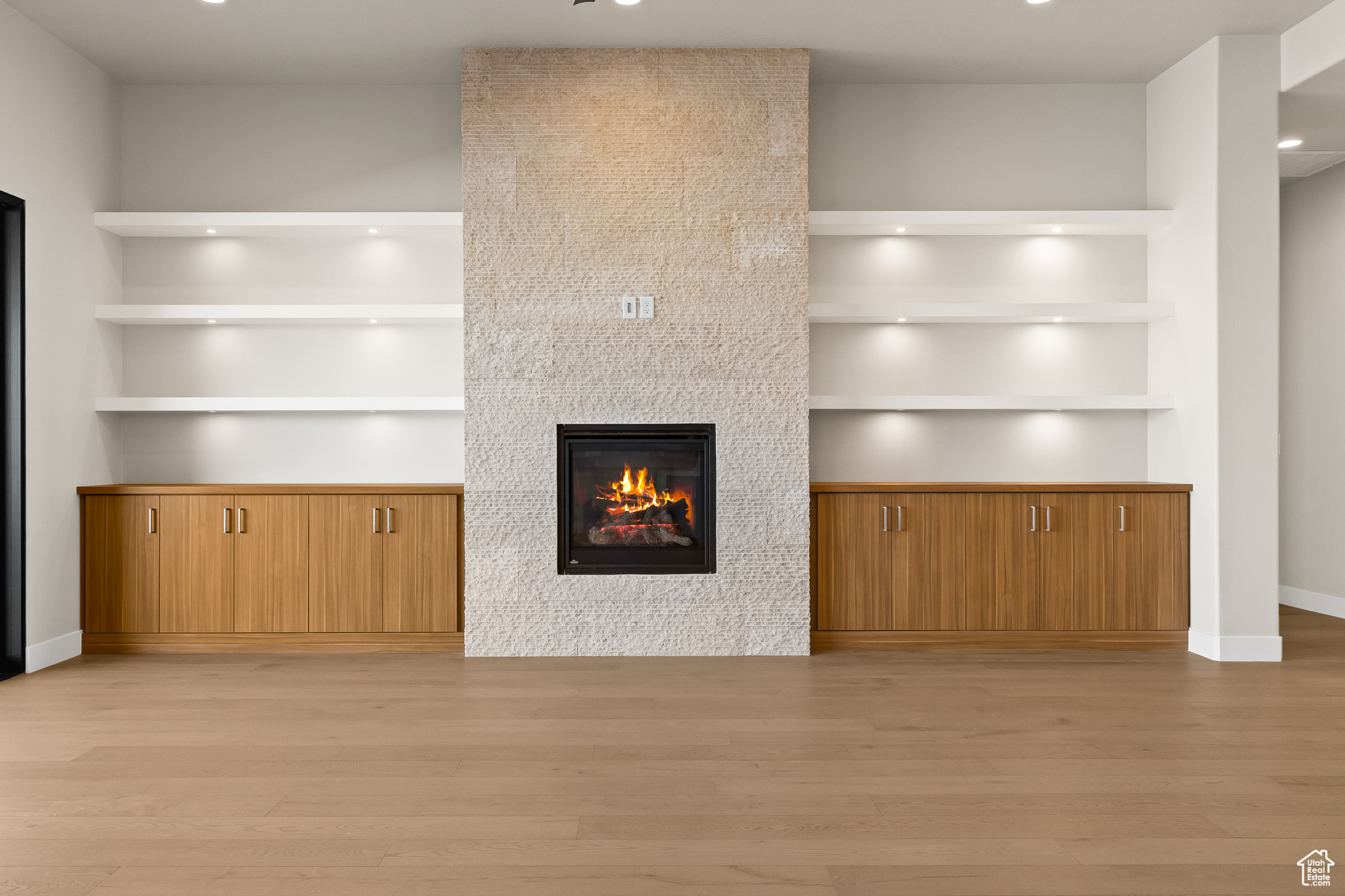 Unfurnished living room featuring a tiled fireplace, built in shelves, baseboards, and light wood-style floors