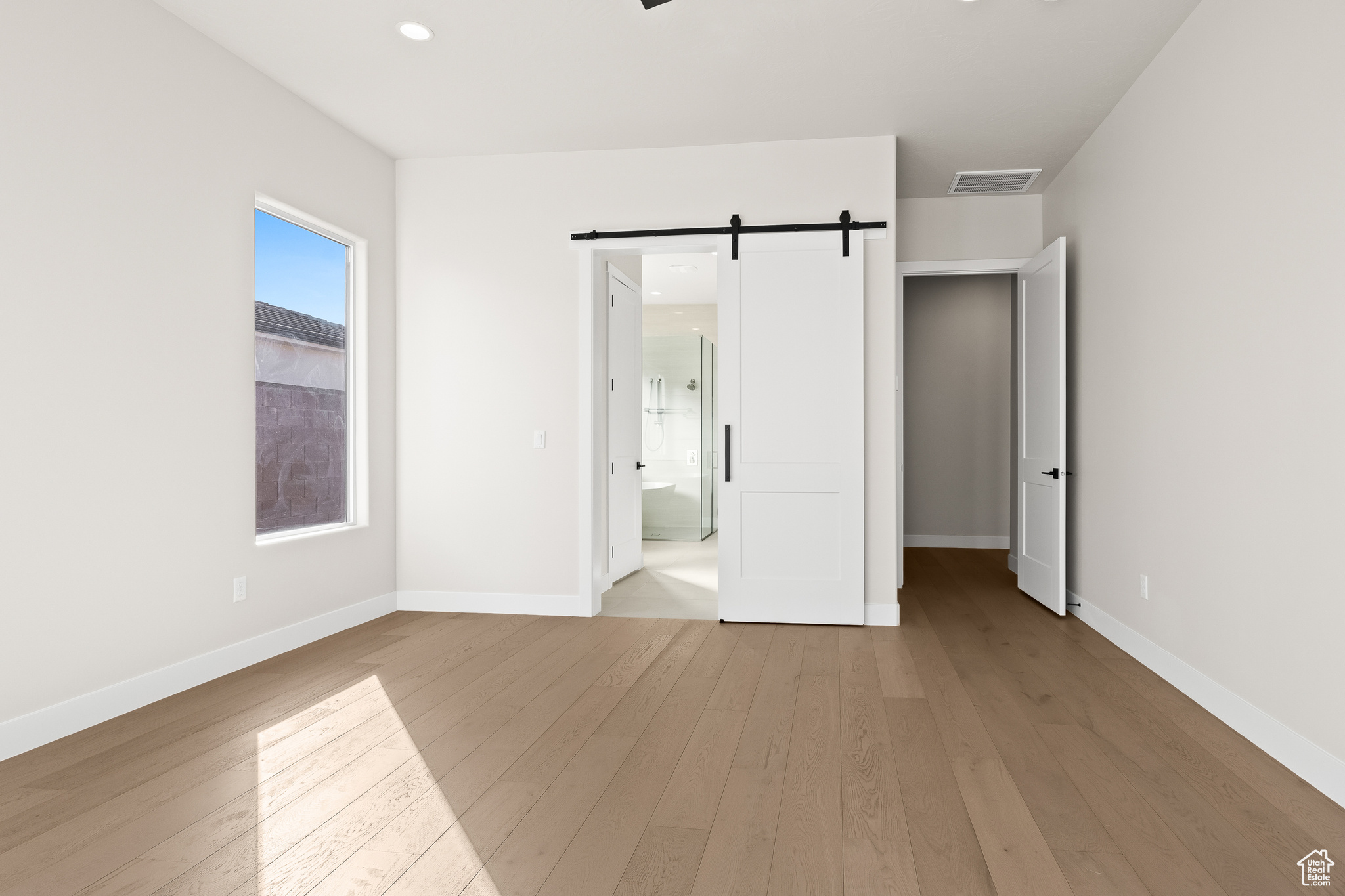 Unfurnished bedroom featuring a barn door, baseboards, visible vents, and hardwood / wood-style flooring