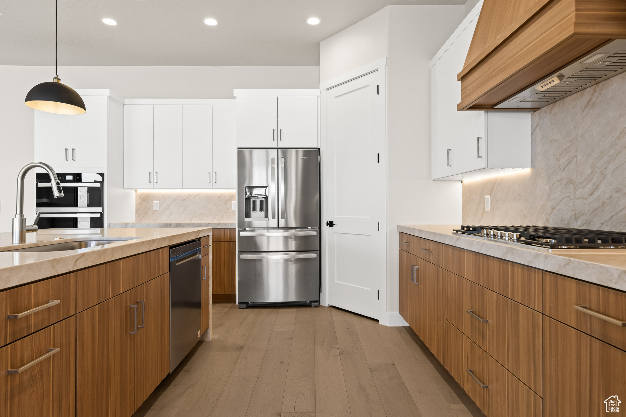 Kitchen with premium range hood, light wood finished floors, a sink, white cabinets, and appliances with stainless steel finishes