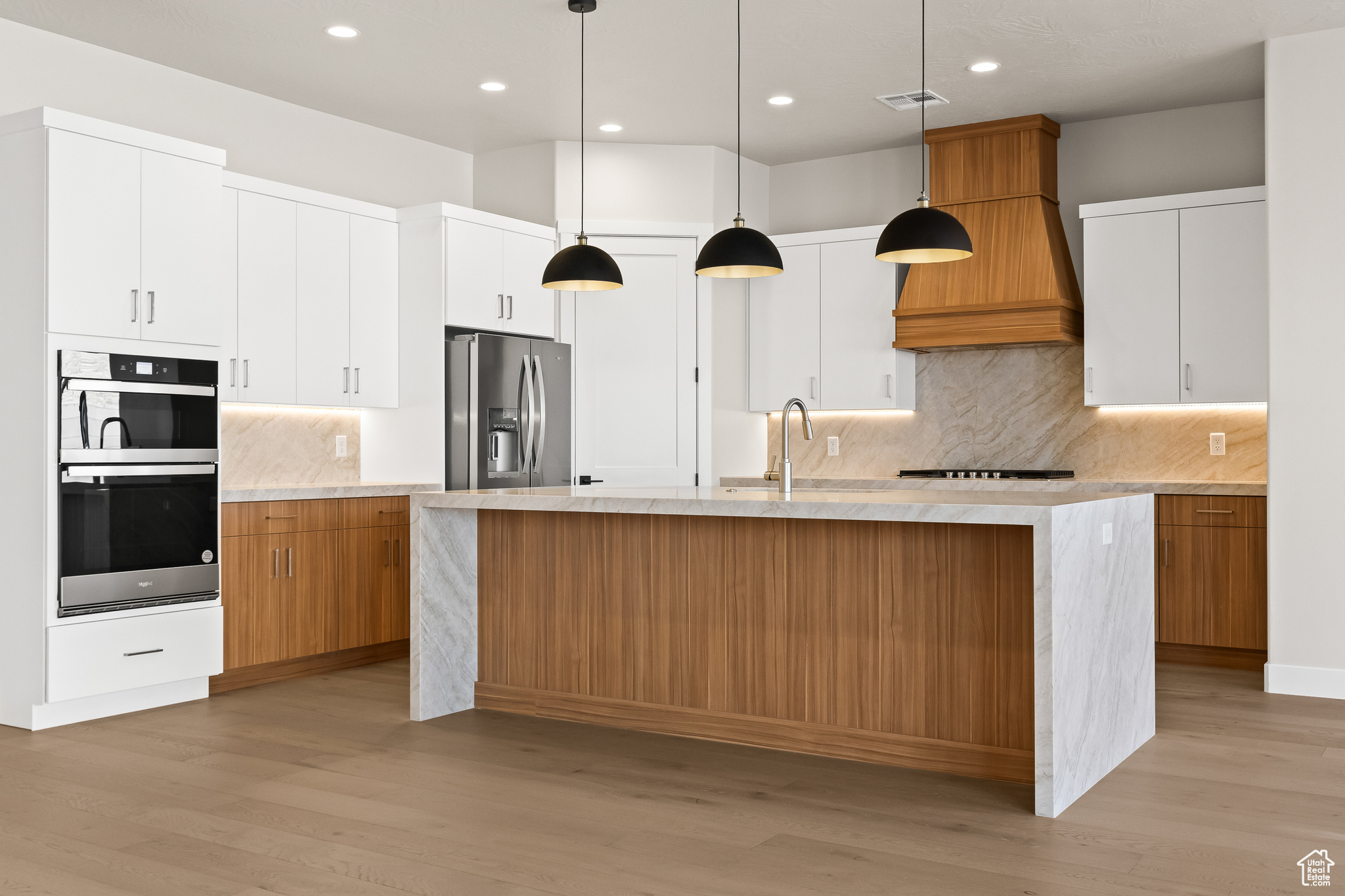 Kitchen with a center island with sink, visible vents, light wood-style flooring, a sink, and stainless steel refrigerator with ice dispenser