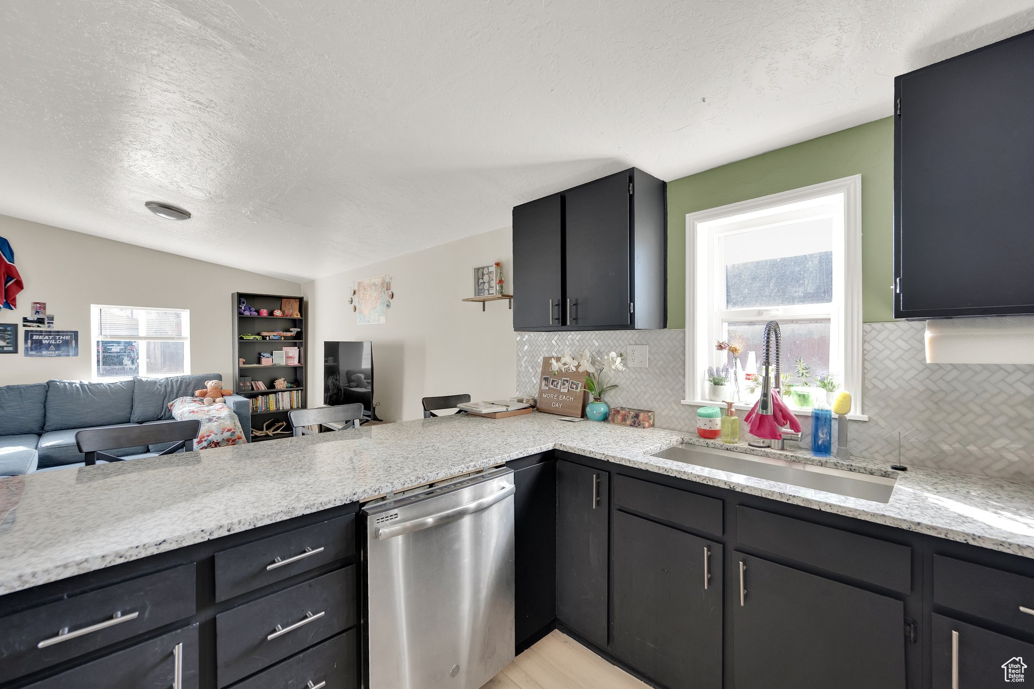 Kitchen with lofted ceiling, sink, stainless steel dishwasher, kitchen peninsula, and light stone countertops