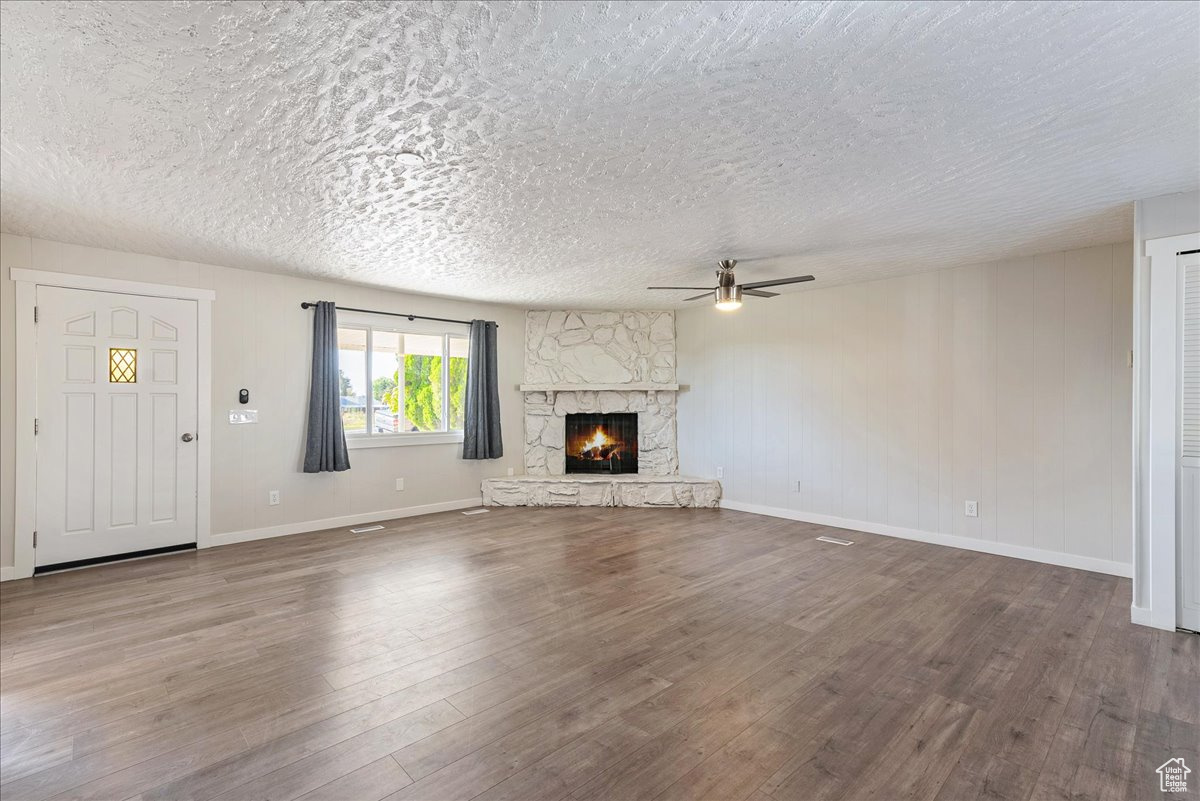 Unfurnished living room with ceiling fan, a textured ceiling, a fireplace, and wood-type flooring