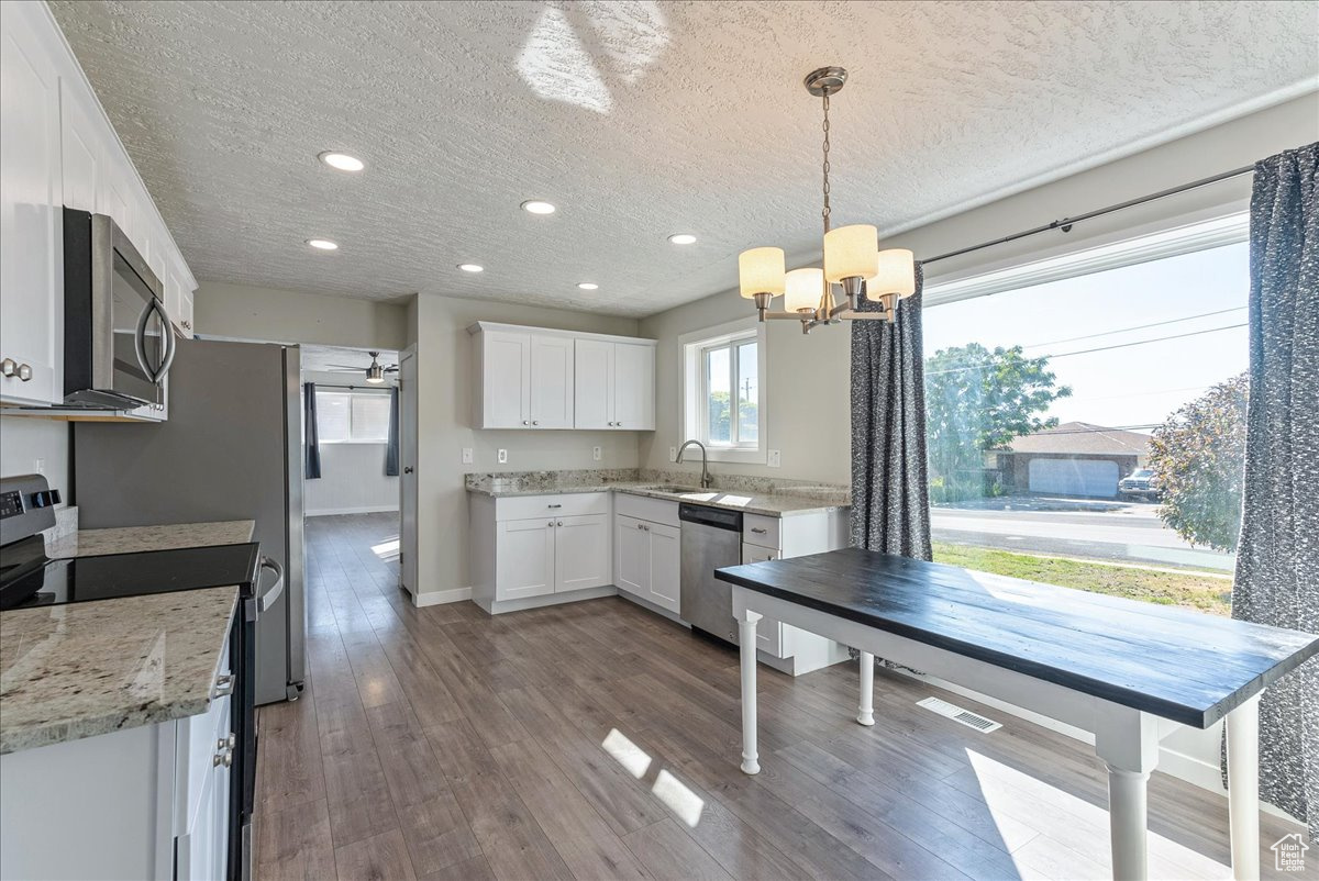 Kitchen featuring appliances with stainless steel finishes, pendant lighting, sink, white cabinets, and light hardwood / wood-style floors