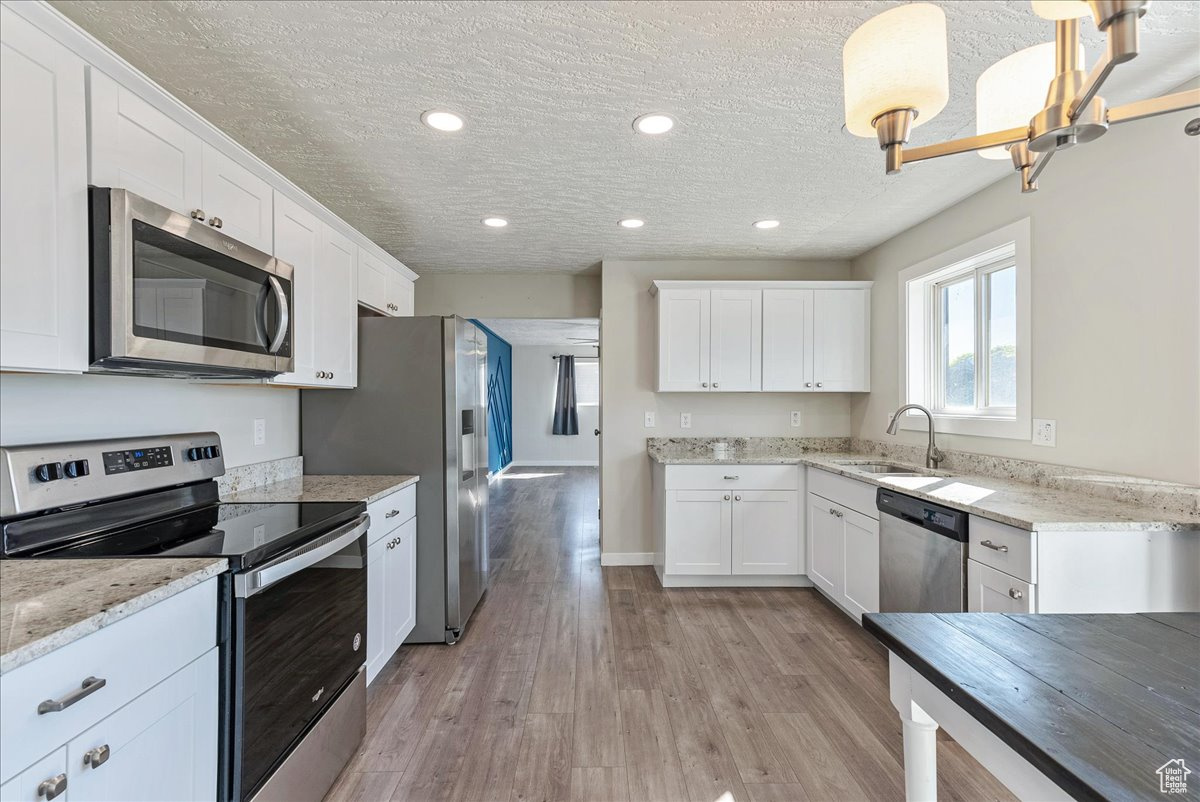 Kitchen with pendant lighting, sink, appliances with stainless steel finishes, white cabinetry, and light wood-type flooring