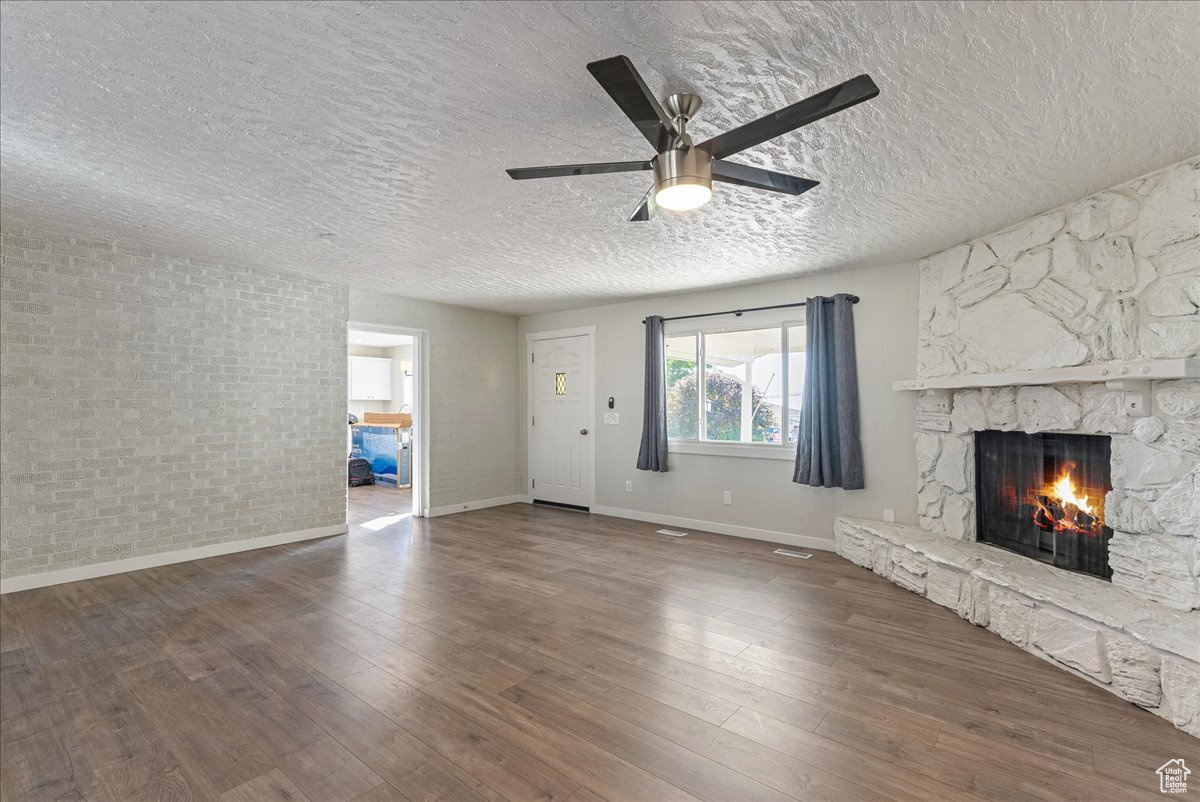 Unfurnished living room featuring a stone fireplace, wood-type flooring, a textured ceiling, and ceiling fan