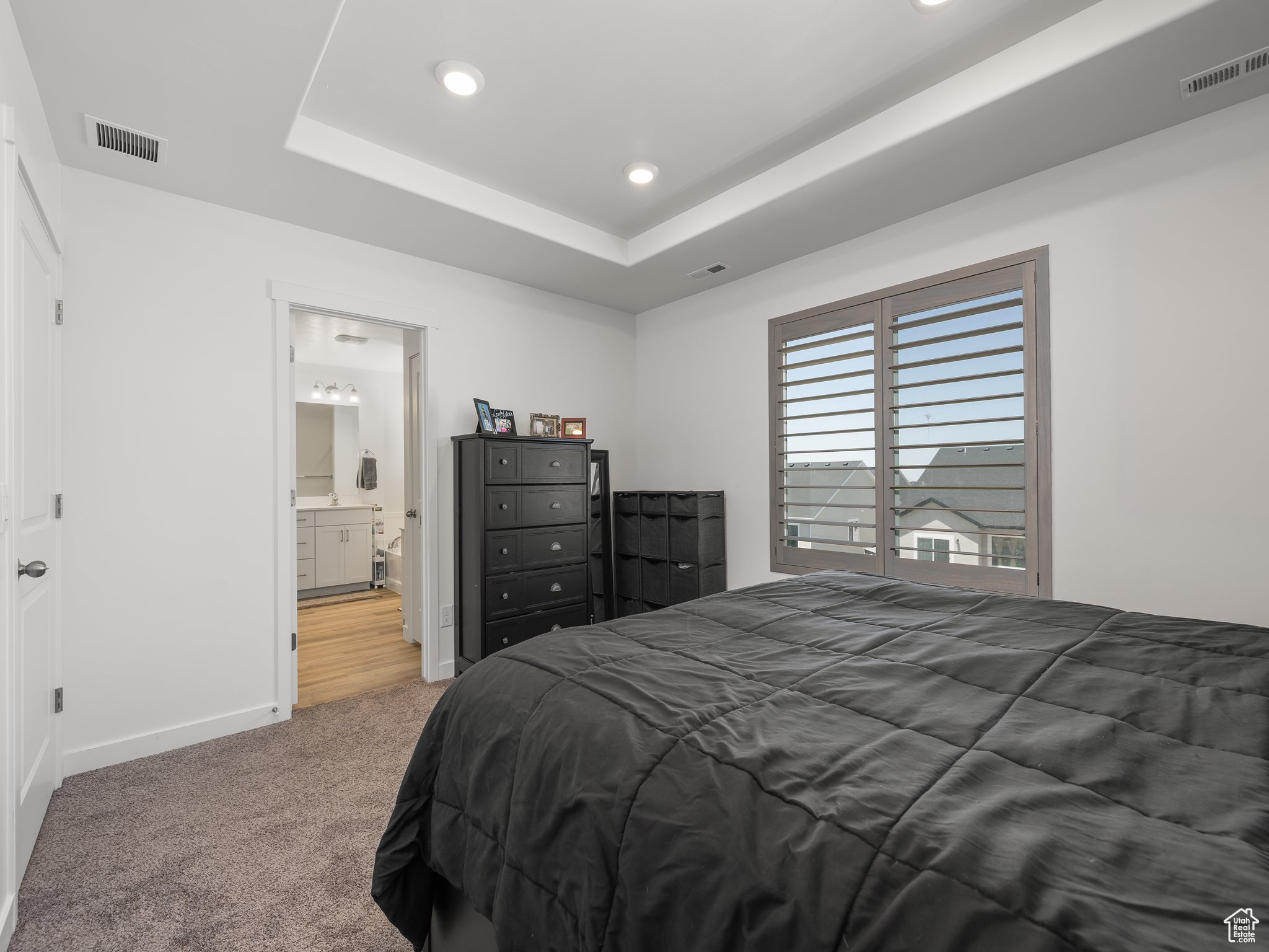 Carpeted bedroom featuring a raised ceiling and ensuite bath