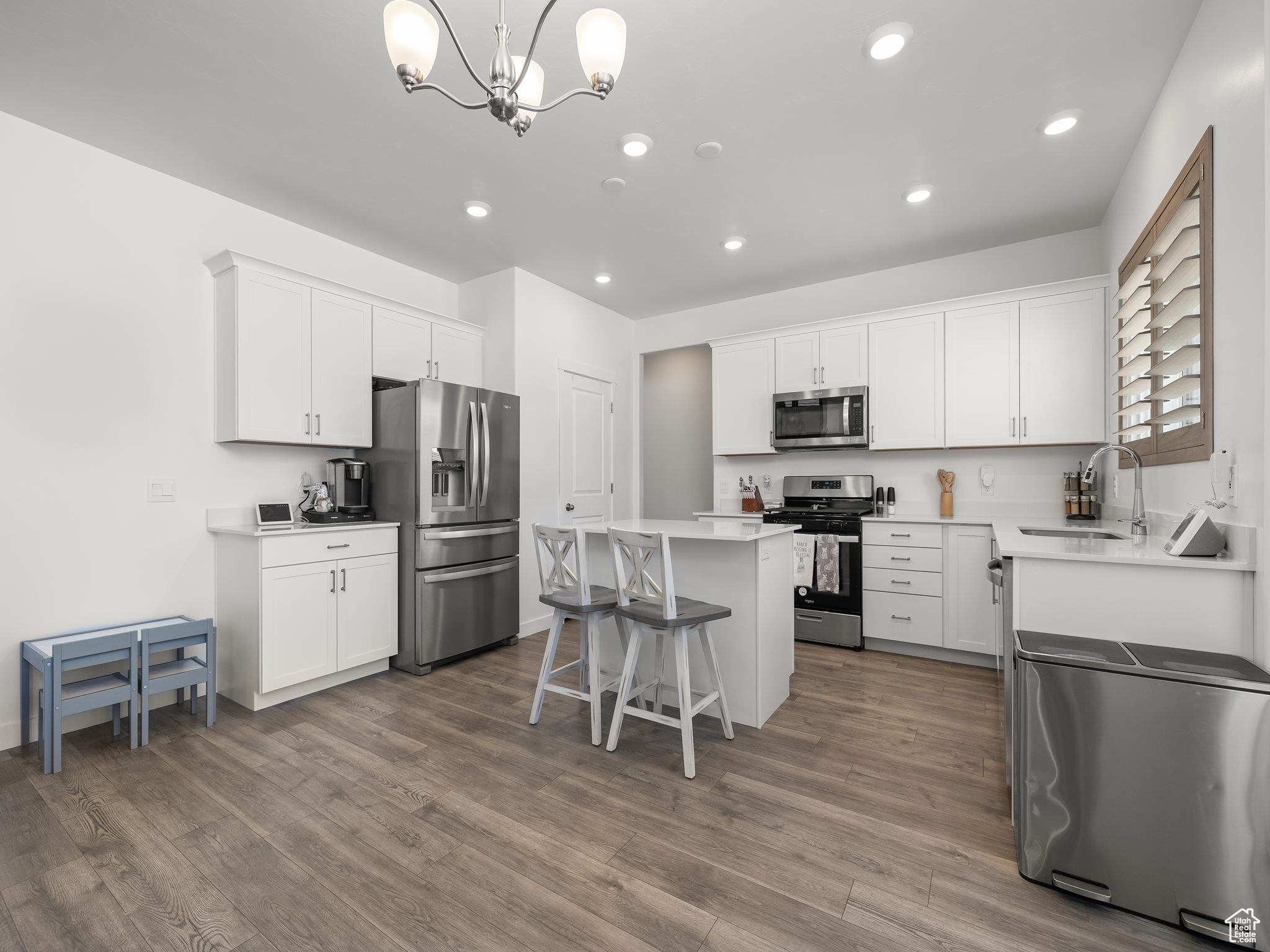 Kitchen featuring sink, appliances with stainless steel finishes, a kitchen island, pendant lighting, and white cabinets