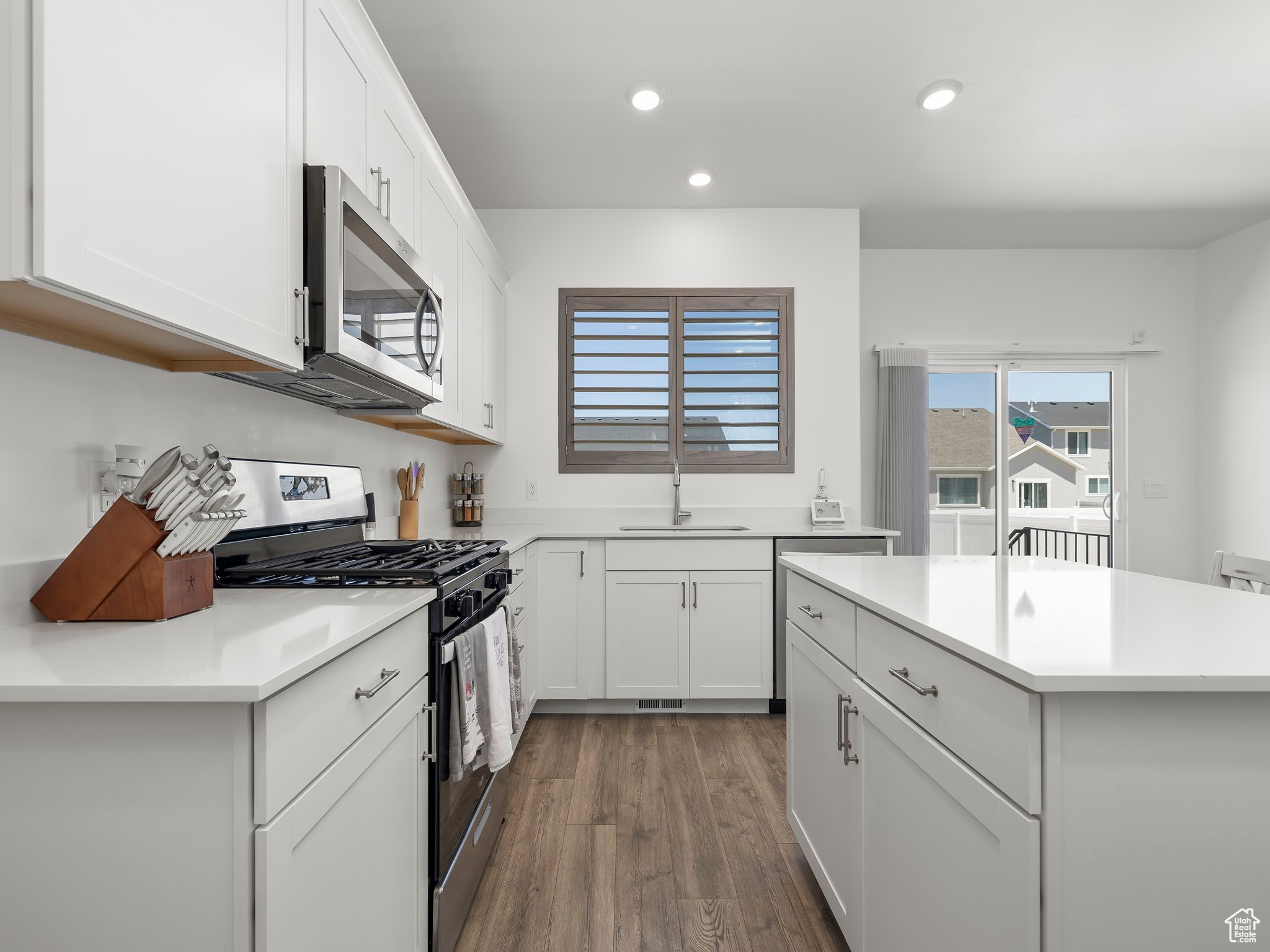 Kitchen with a kitchen island, sink, white cabinets, dark hardwood / wood-style flooring, and stainless steel appliances