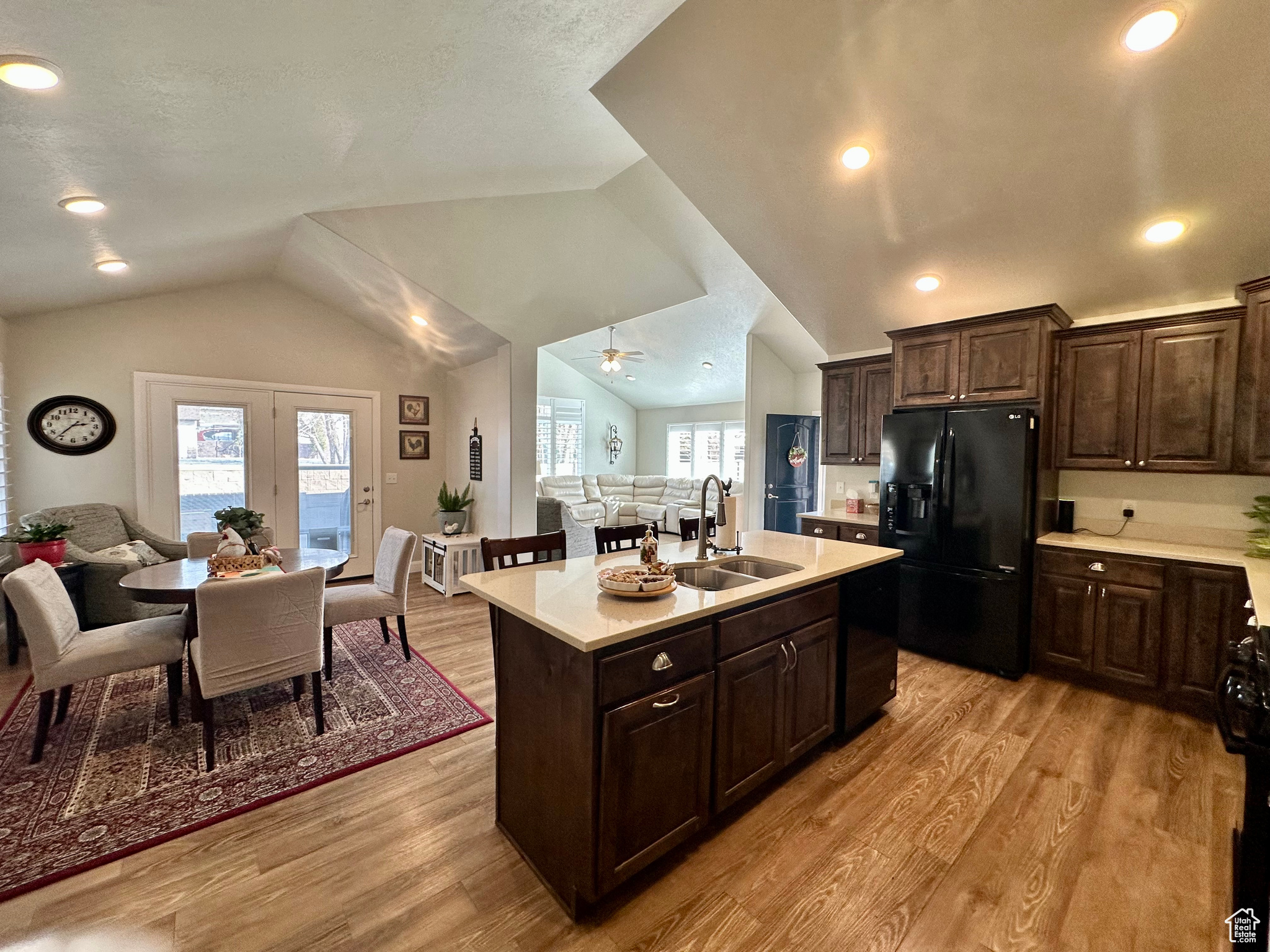 Kitchen featuring open floor plan, vaulted ceiling, black fridge, light countertops, and a sink