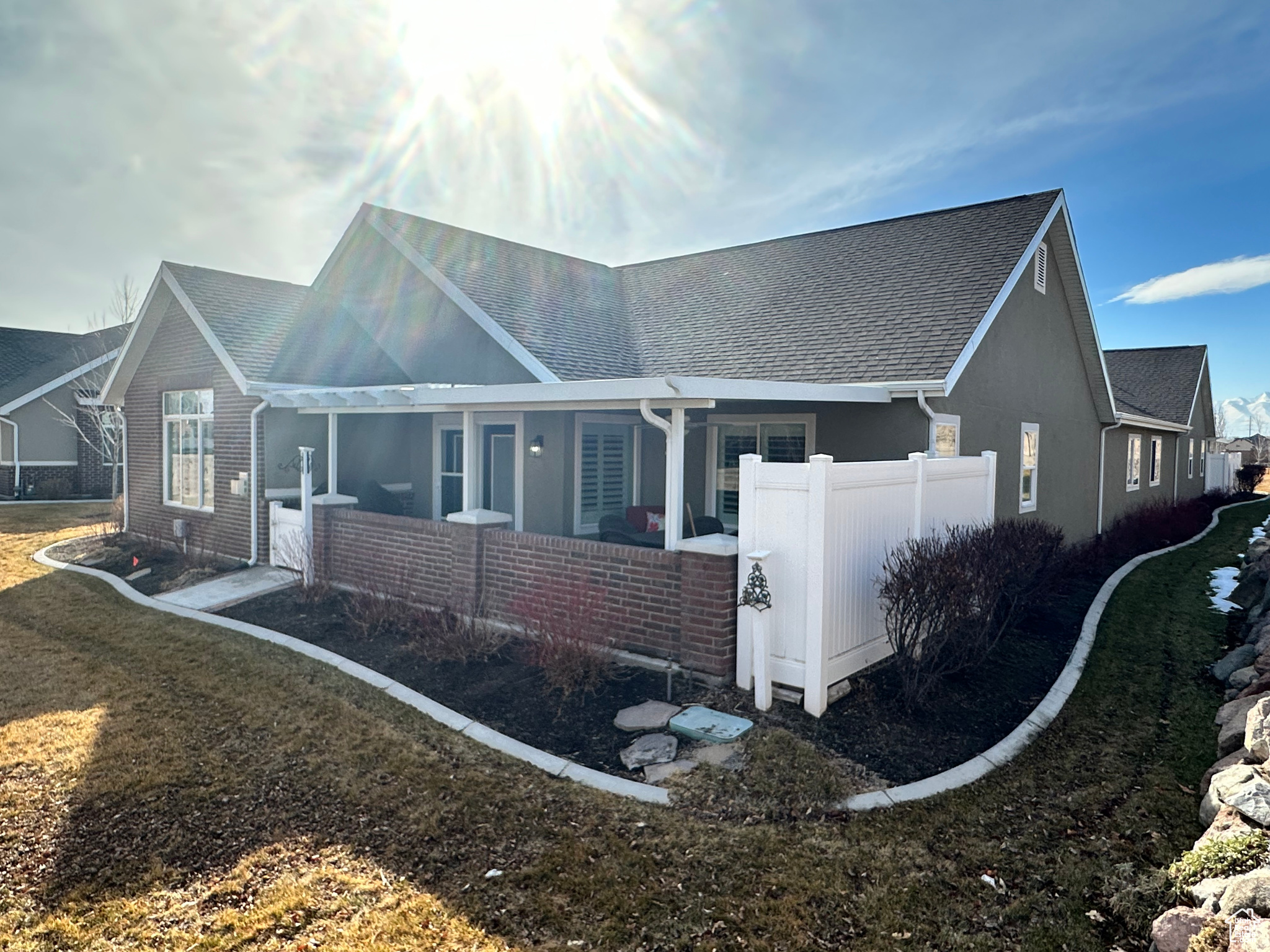 View of front of house featuring a shingled roof, brick siding, fence, and stucco siding