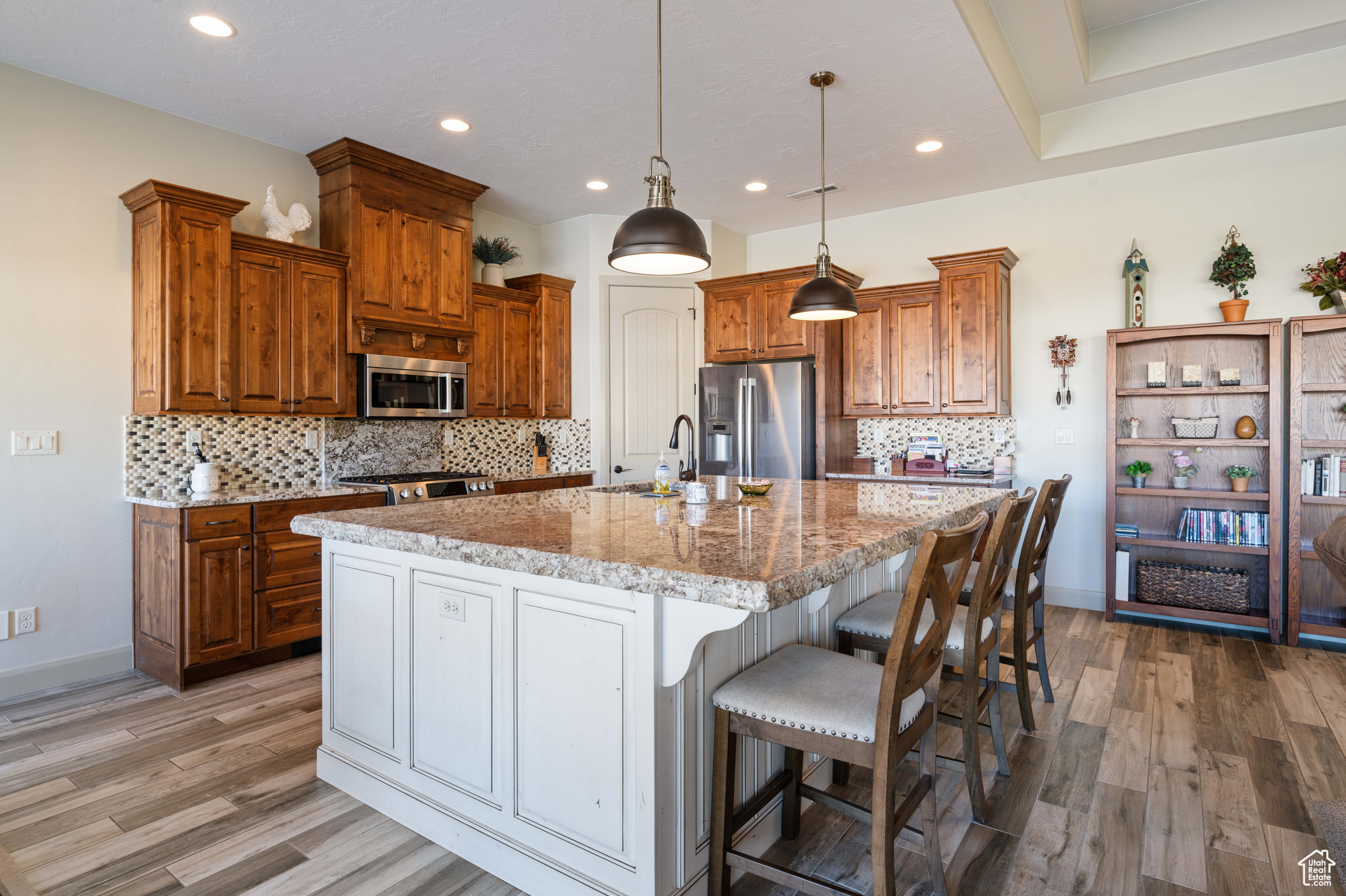 Kitchen with appliances with stainless steel finishes, pendant lighting, an island with sink, sink, and light stone counters