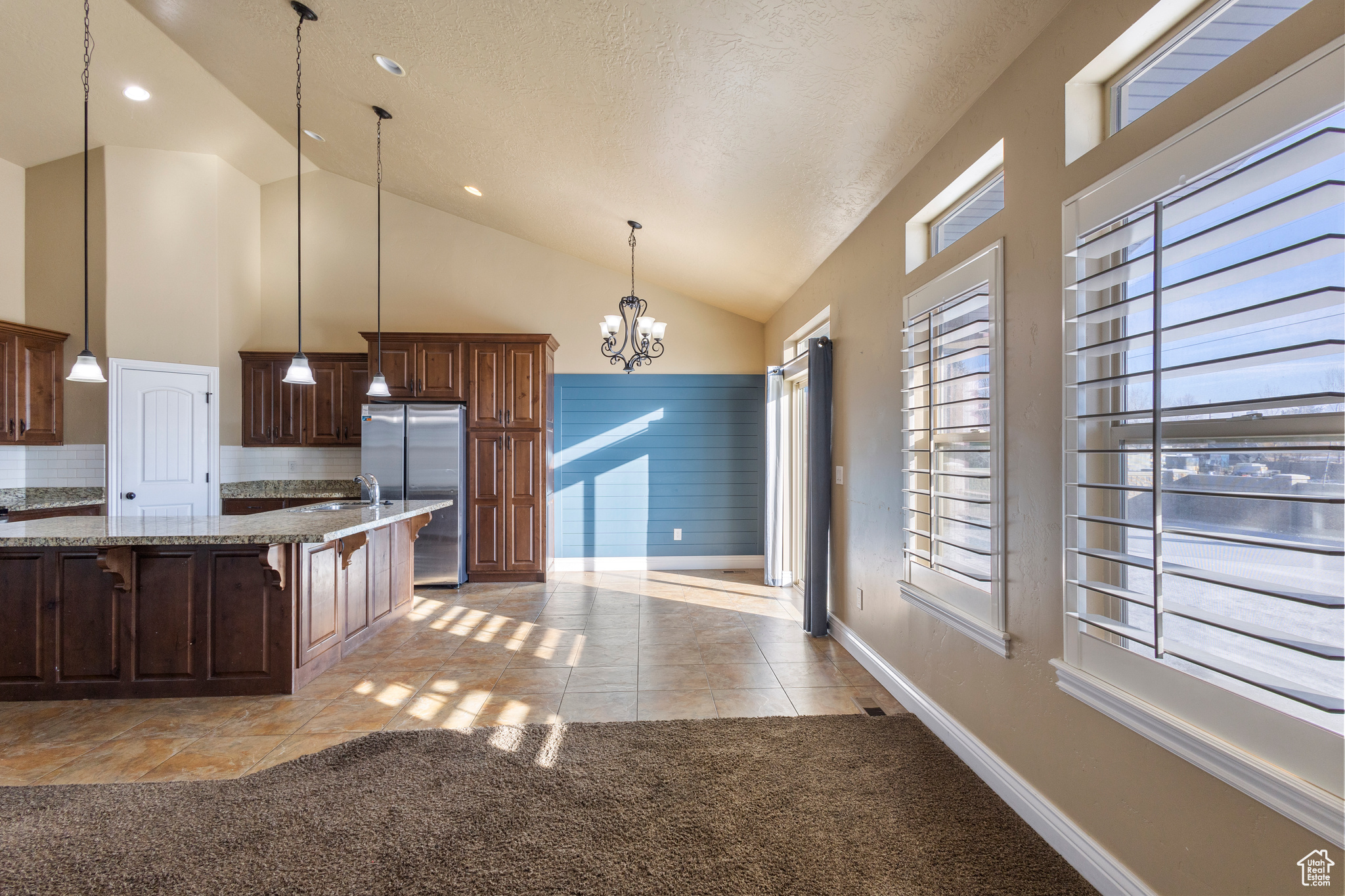 Kitchen with light tile patterned flooring, a breakfast bar area, an inviting chandelier, decorative light fixtures, and stainless steel refrigerator