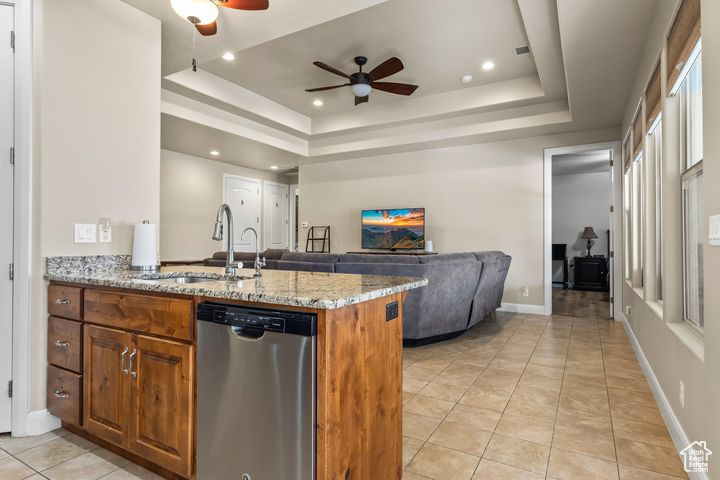 Kitchen with sink, a tray ceiling, kitchen peninsula, dishwasher, and light stone countertops