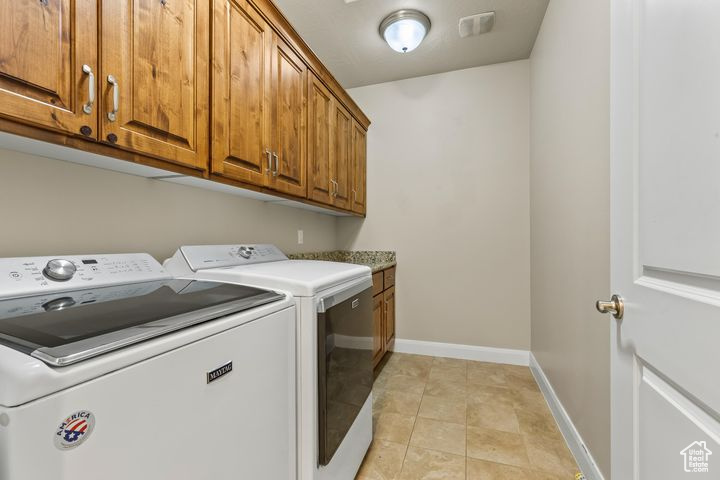 Washroom featuring cabinets, washing machine and dryer, and light tile patterned floors