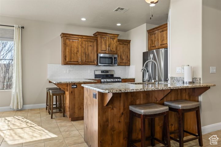 Kitchen with appliances with stainless steel finishes, a breakfast bar area, light stone counters, and kitchen peninsula