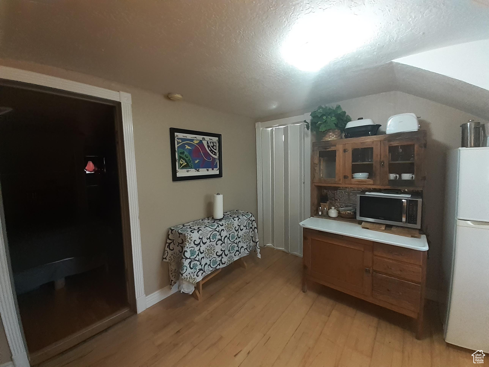 Kitchen with a textured ceiling, light hardwood / wood-style flooring, vaulted ceiling, and white refrigerator