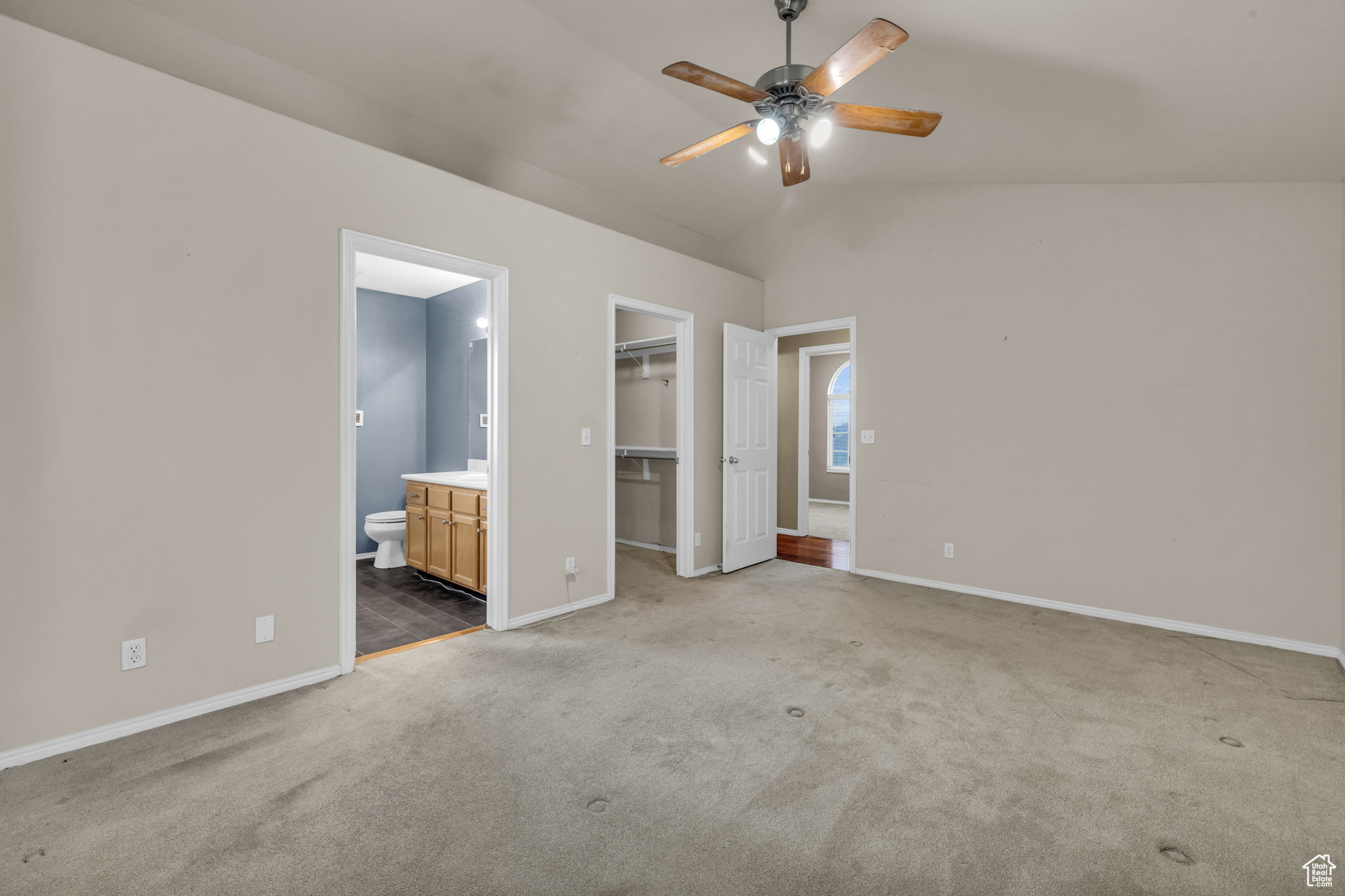 Unfurnished bedroom with a walk in closet, light colored carpet, ensuite bathroom, and vaulted ceiling