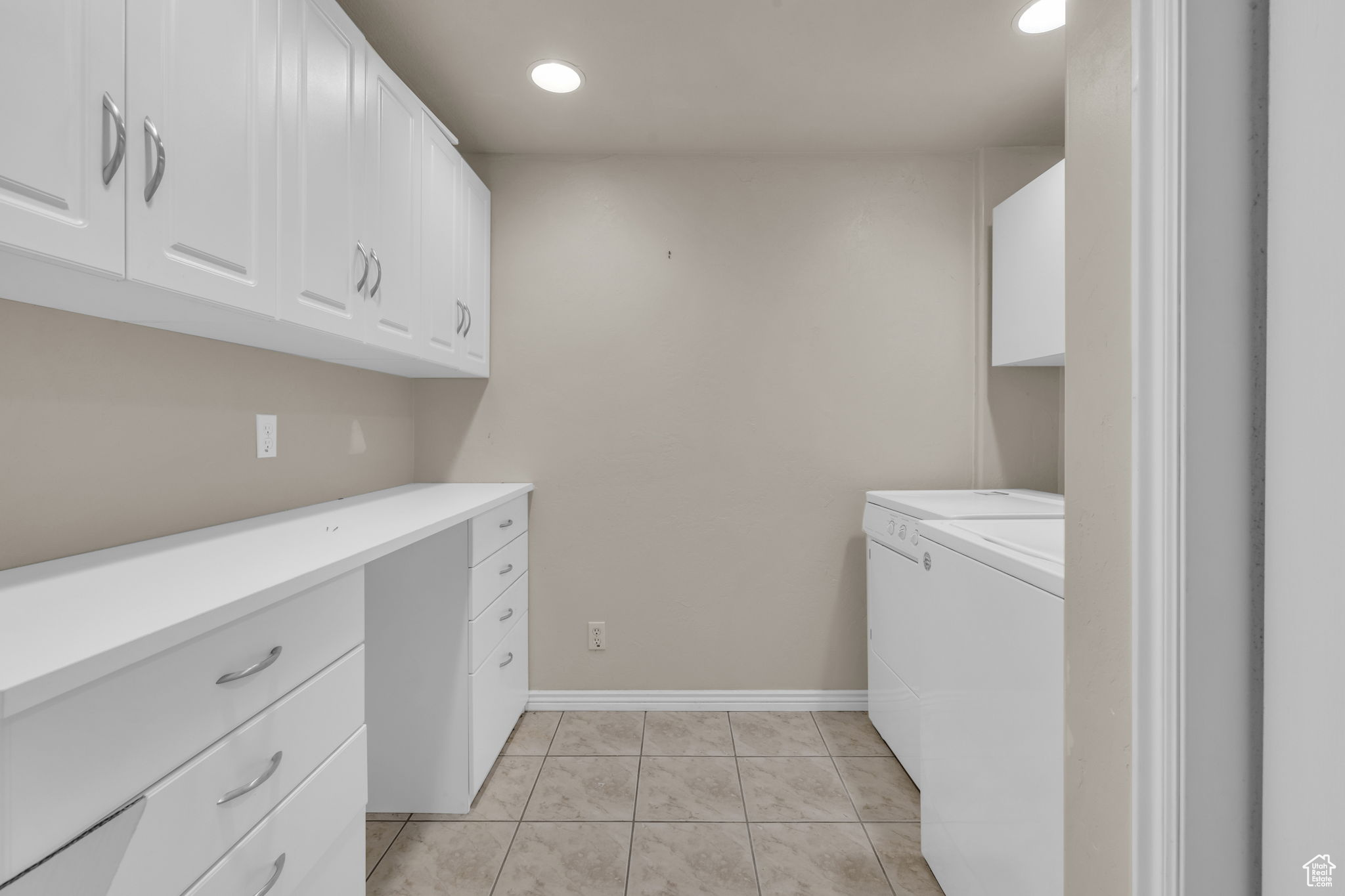 Clothes washing area with separate washer and dryer, light tile patterned floors, and cabinets