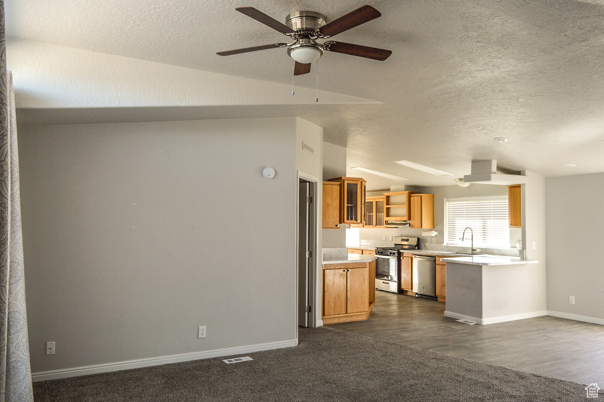 Kitchen with lofted ceiling, sink, appliances with stainless steel finishes, a textured ceiling, and new laminate flooring plus updated carpet.