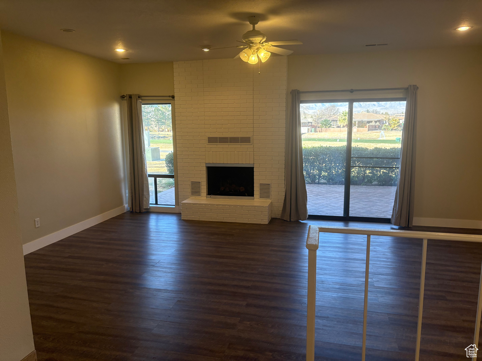 Unfurnished living room featuring dark wood-type flooring, ceiling fan, and a fireplace