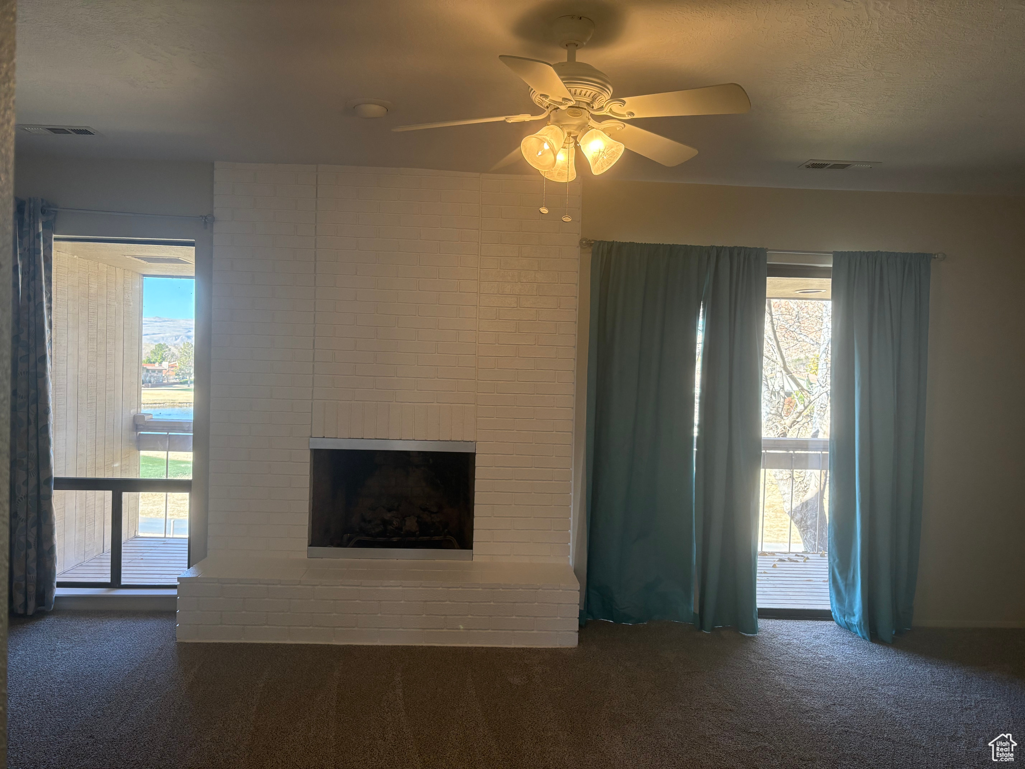 Unfurnished living room featuring ceiling fan, a fireplace, a textured ceiling, and dark colored carpet