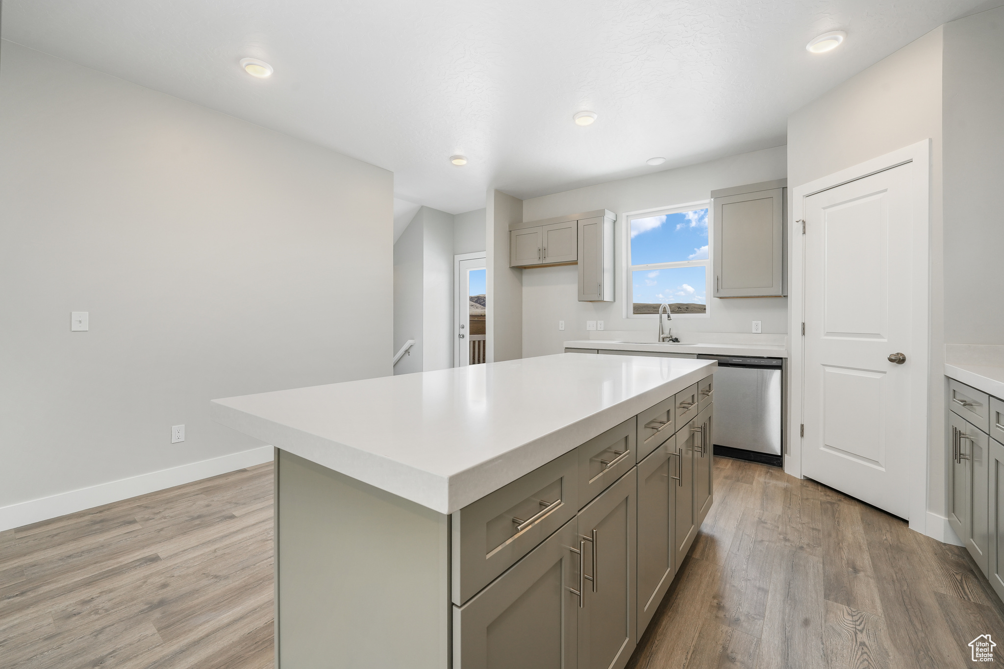 Kitchen with gray cabinetry, light hardwood / wood-style flooring, stainless steel dishwasher, and a center island