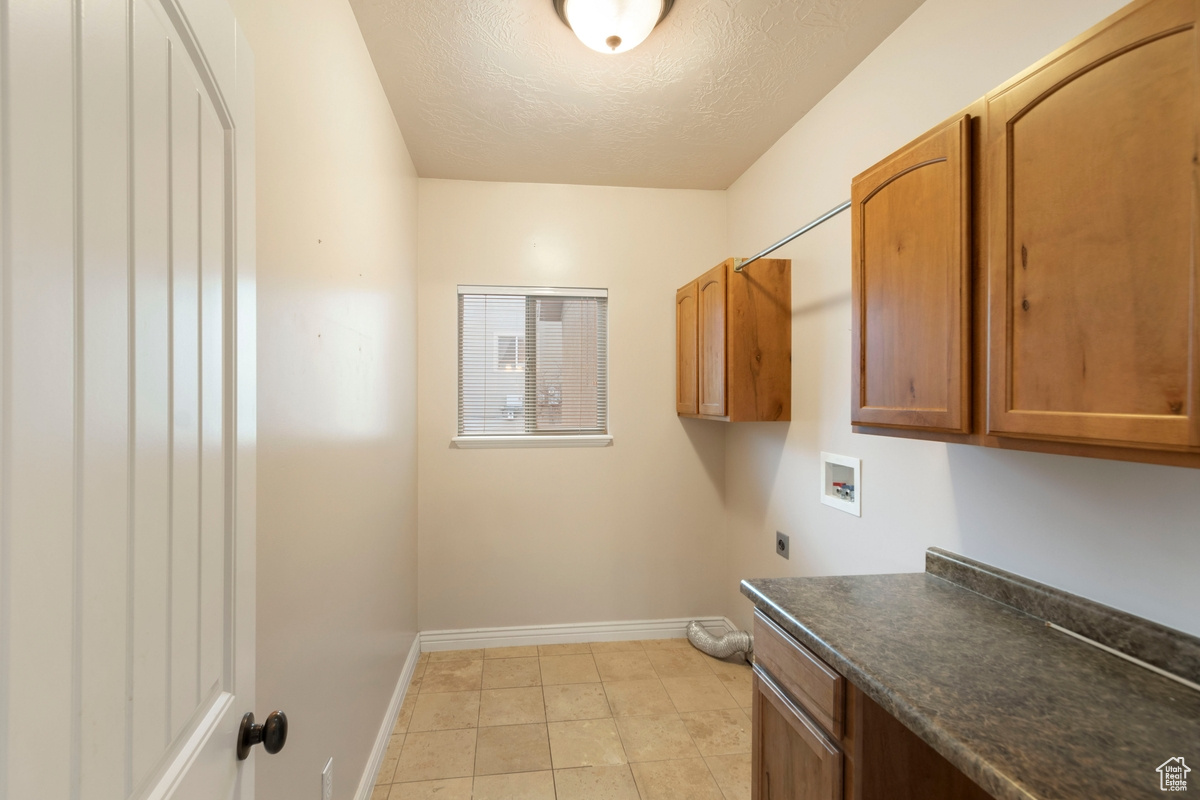 Laundry room with light tile patterned flooring, cabinets, a textured ceiling, washer hookup, and hookup for an electric dryer