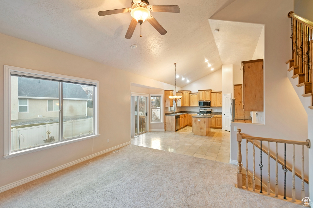 Living room featuring ceiling fan with notable chandelier, lofted ceiling, and light colored carpet
