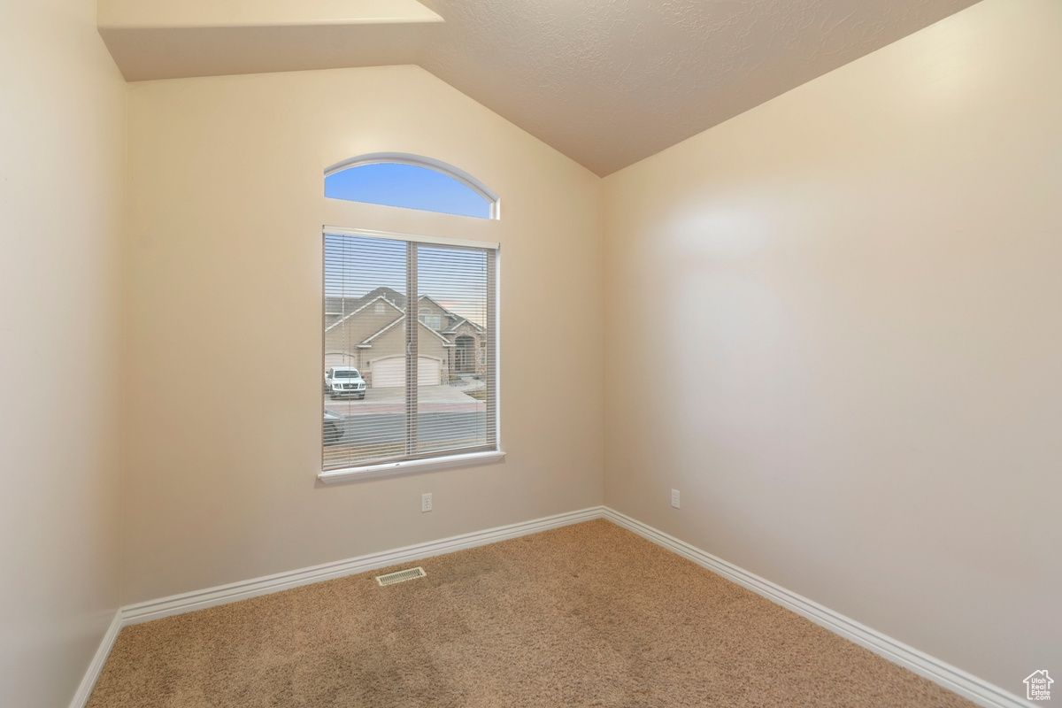 Carpeted empty room featuring vaulted ceiling