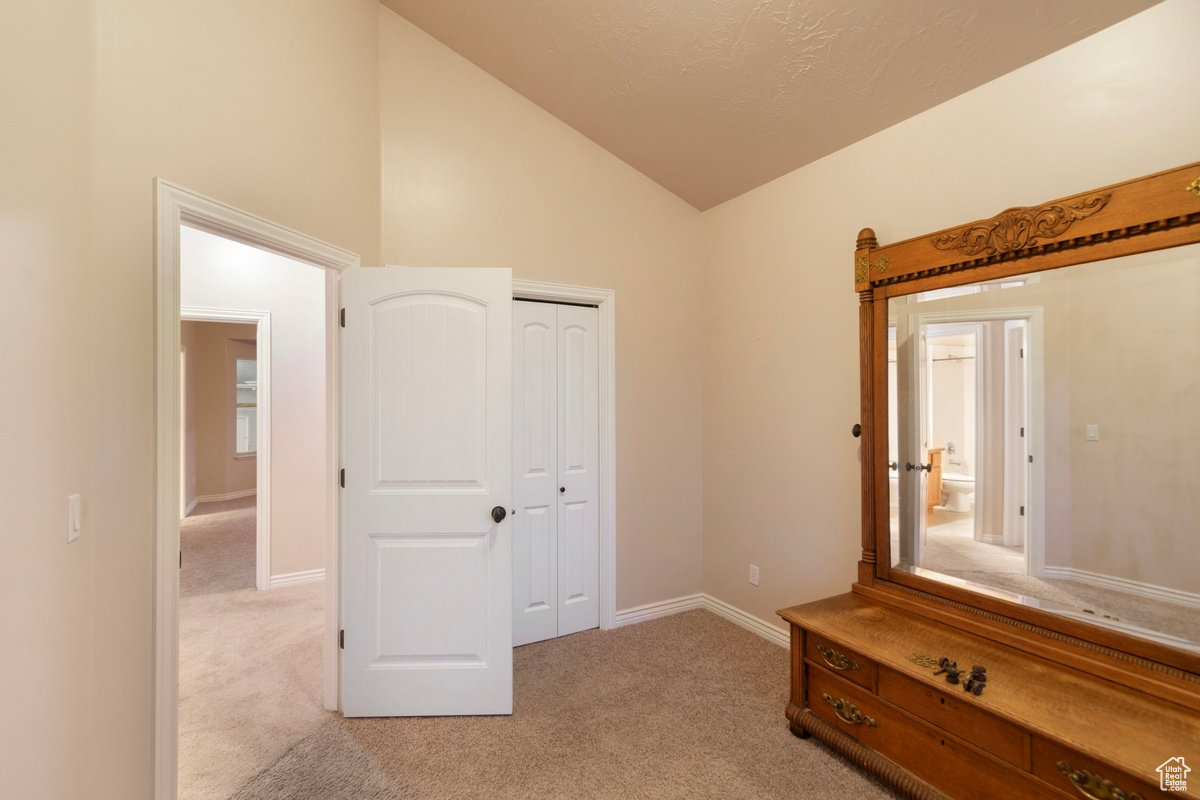 Unfurnished bedroom featuring vaulted ceiling, light colored carpet, and a closet
