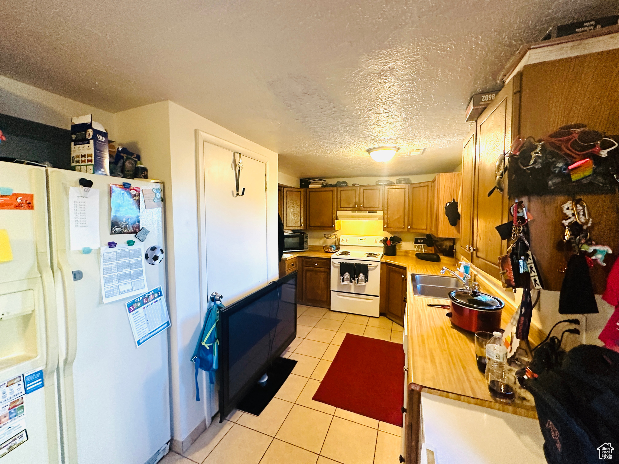 Kitchen featuring sink, white appliances, light tile patterned floors, and a textured ceiling