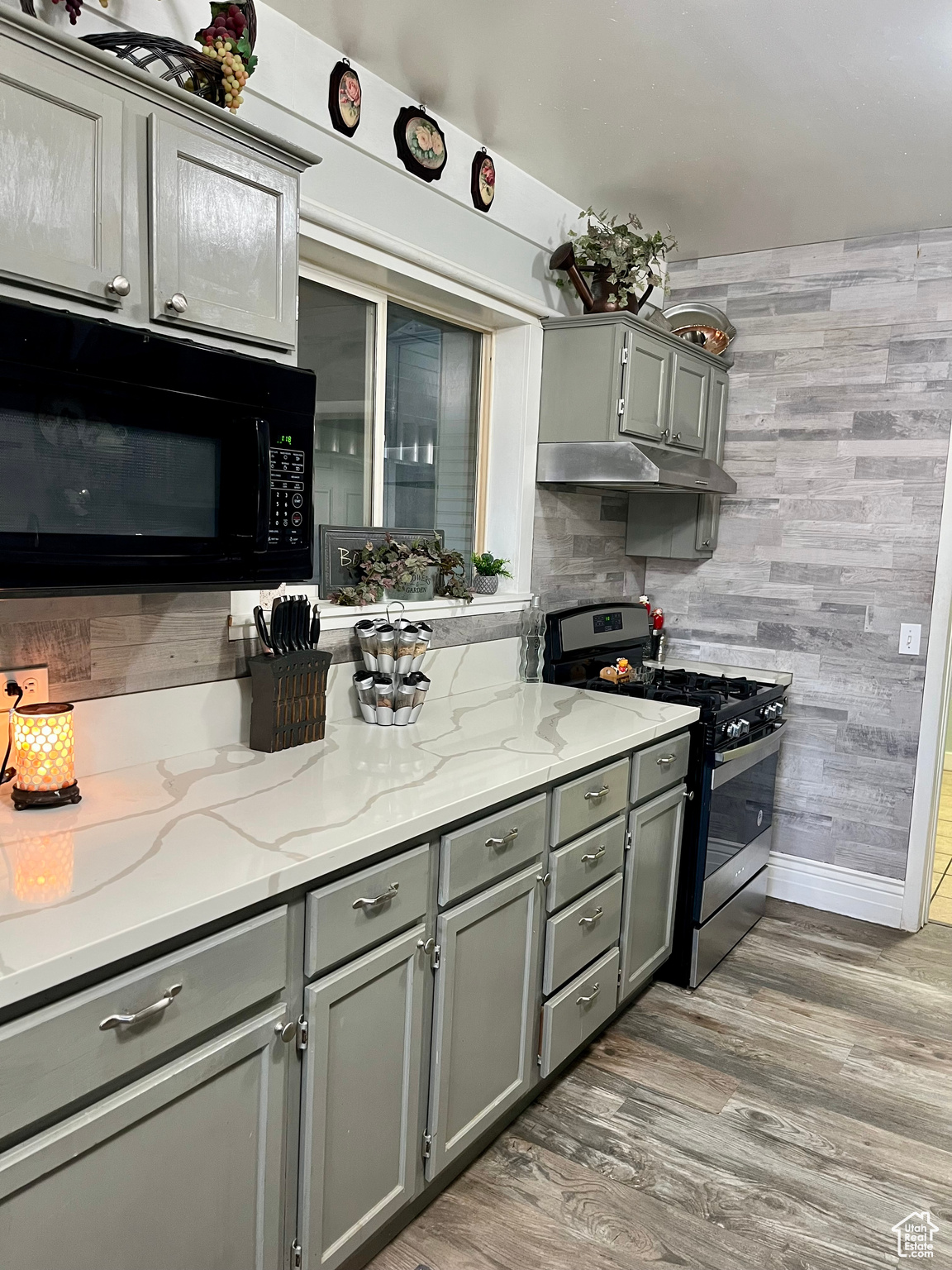Kitchen featuring hardwood / wood-style floors, stainless steel gas range oven, light stone countertops, and gray cabinetry