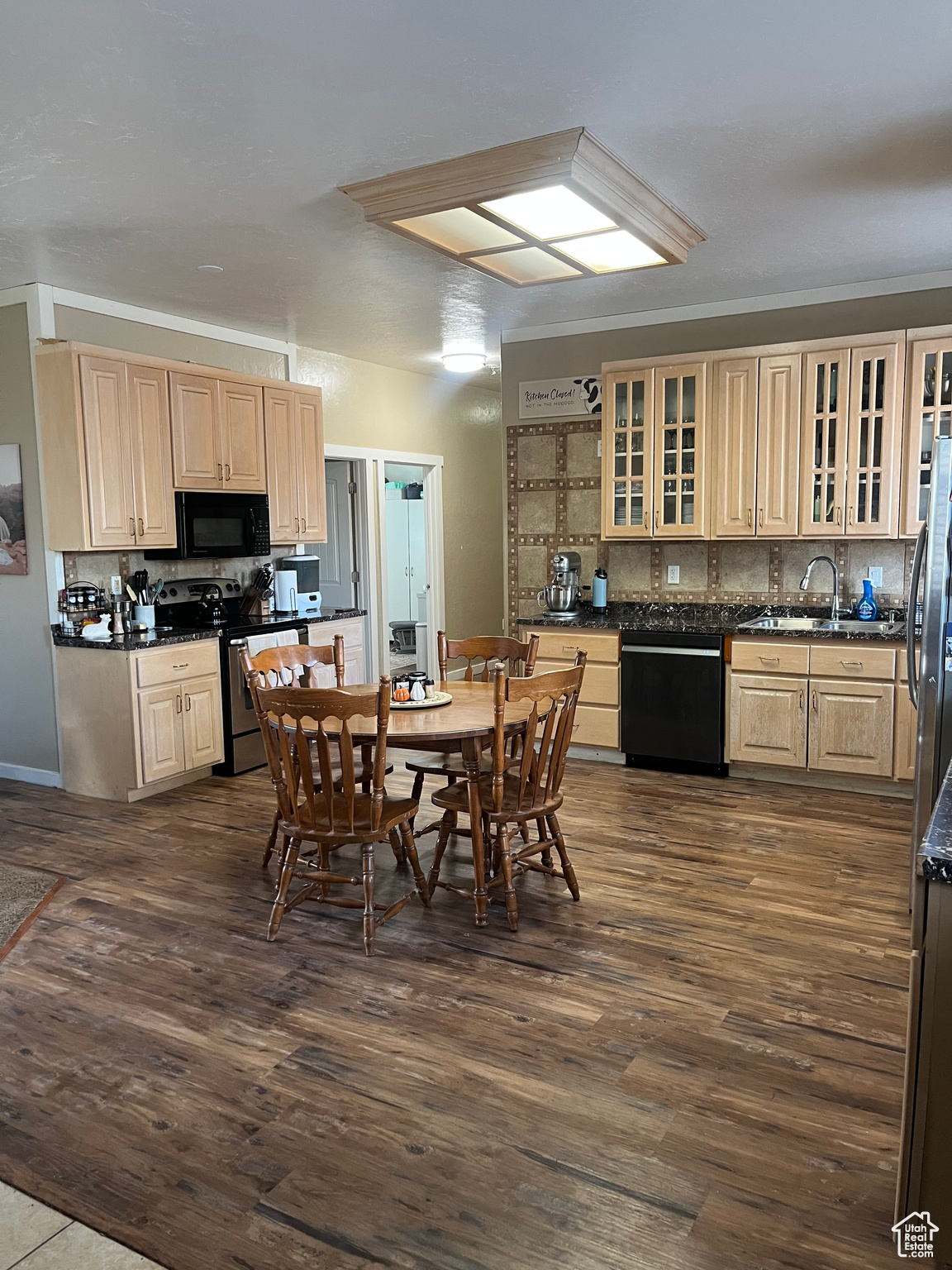 Kitchen with dark wood-type flooring, sink, decorative backsplash, and black appliances