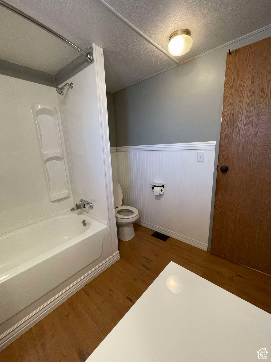Bathroom with hardwood / wood-style flooring, toilet, a textured ceiling, and  shower combination