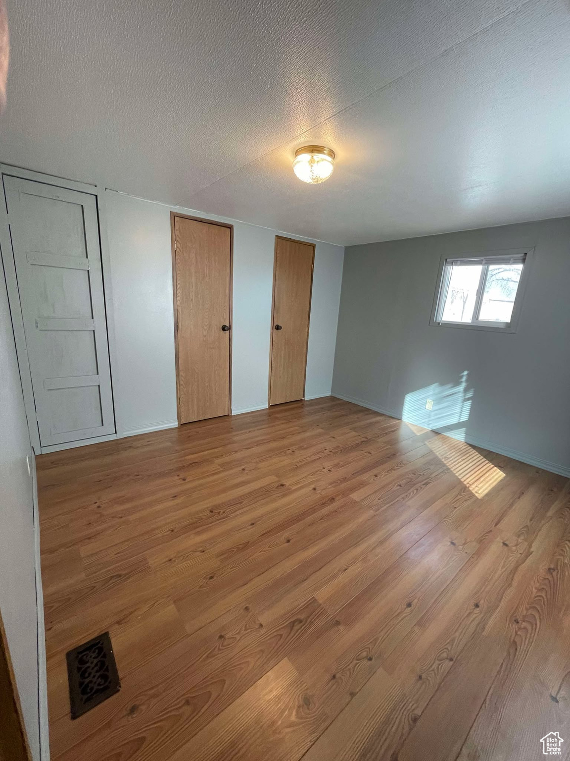 Unfurnished bedroom with multiple closets, light wood-style floors, and a textured ceiling