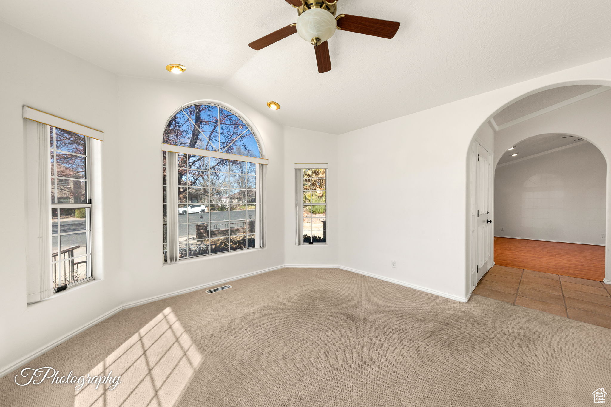 Empty room featuring ceiling fan, light colored carpet, and lofted ceiling