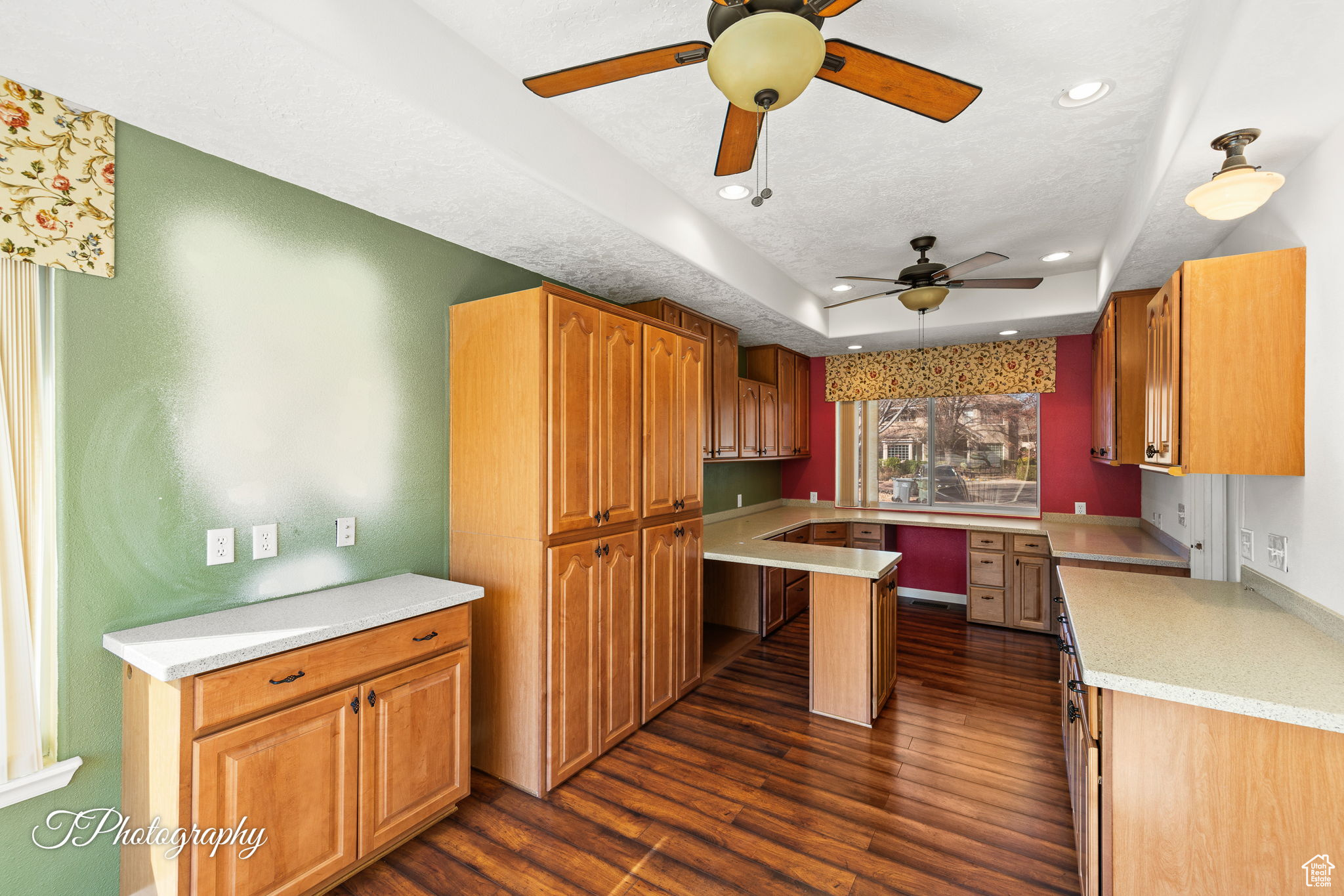 Kitchen with built in desk, ceiling fan, a raised ceiling, dark wood-type flooring, and a textured ceiling