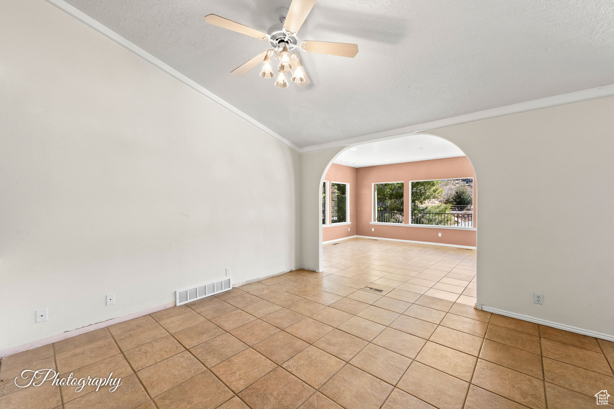 Unfurnished room with vaulted ceiling, light tile patterned floors, ceiling fan, crown molding, and a textured ceiling