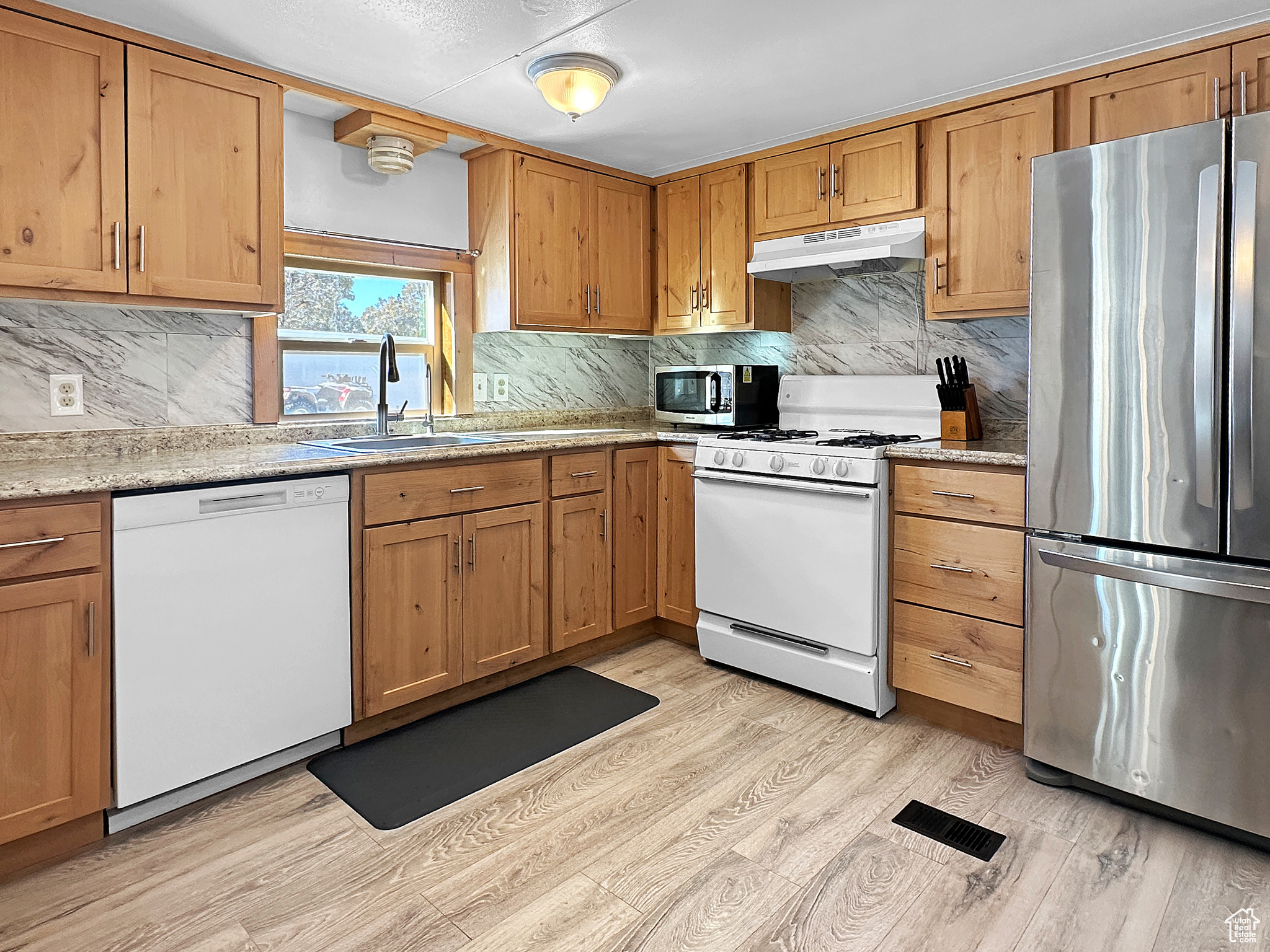 Kitchen with tasteful backsplash, sink, light wood-type flooring, and appliances with stainless steel finishes