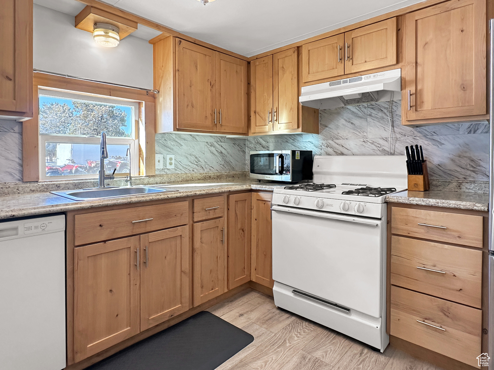 Kitchen featuring white appliances, sink, decorative backsplash, and light hardwood / wood-style flooring