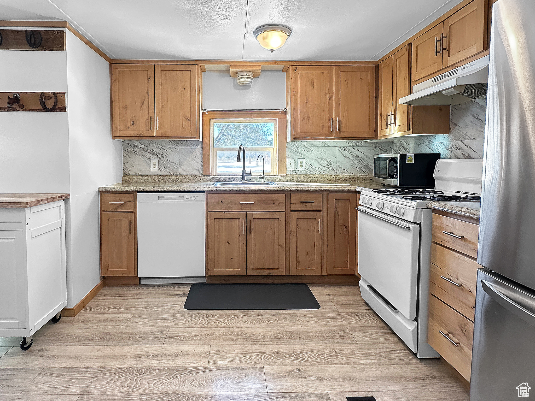 Kitchen featuring sink, light hardwood / wood-style flooring, appliances with stainless steel finishes, tasteful backsplash, and light stone countertops
