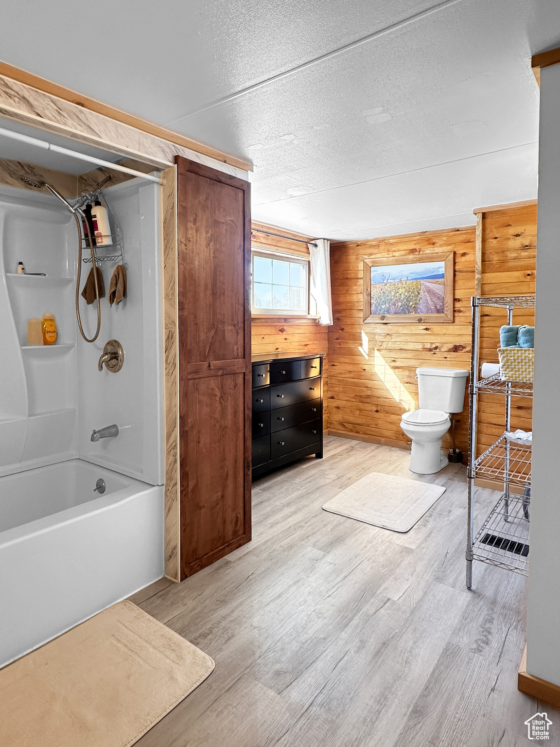 Bathroom featuring shower / tub combination, wood walls, wood-type flooring, toilet, and a textured ceiling