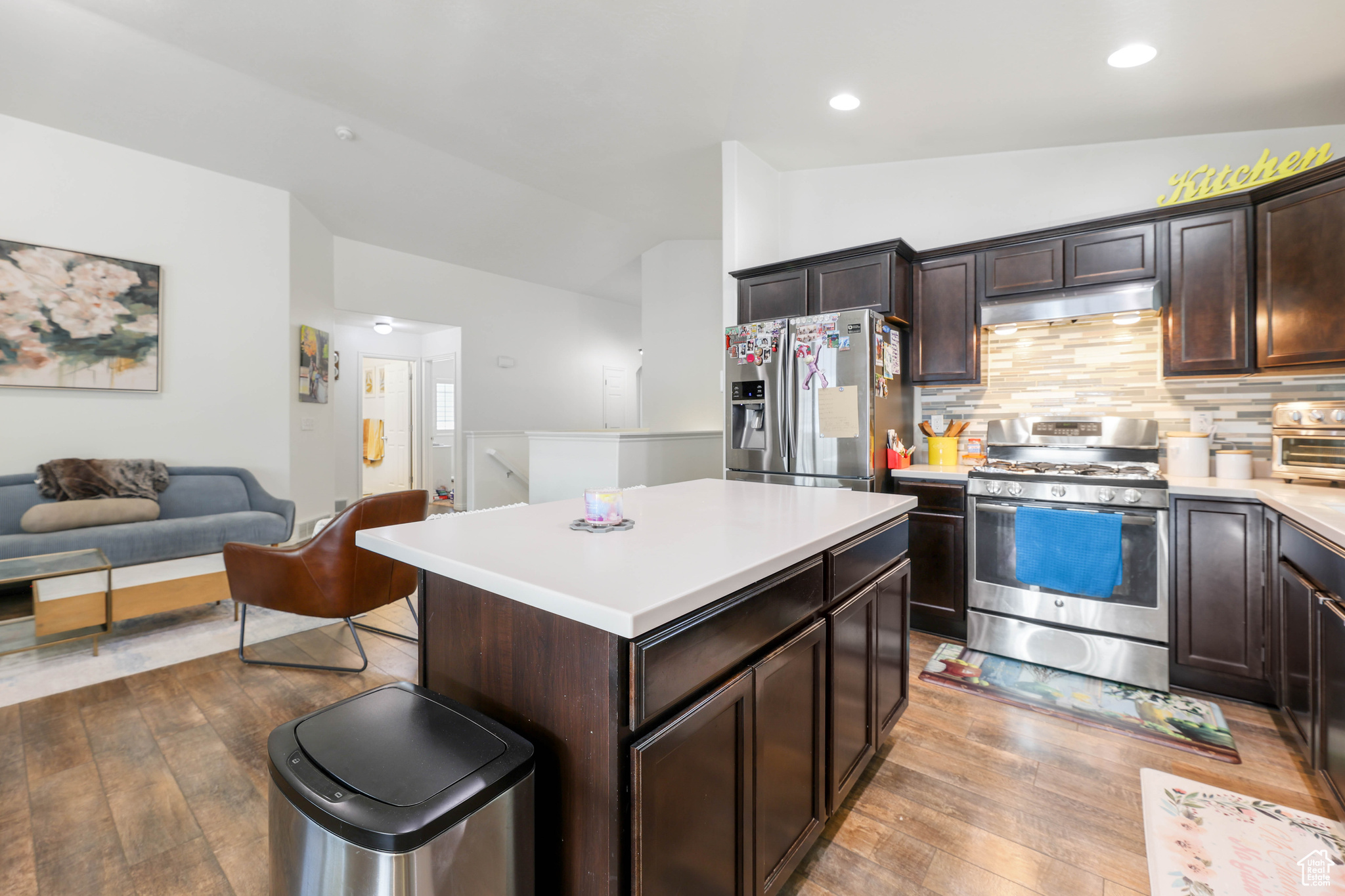 Kitchen featuring lofted ceiling, light hardwood / wood-style flooring, appliances with stainless steel finishes, dark brown cabinets, and a kitchen island